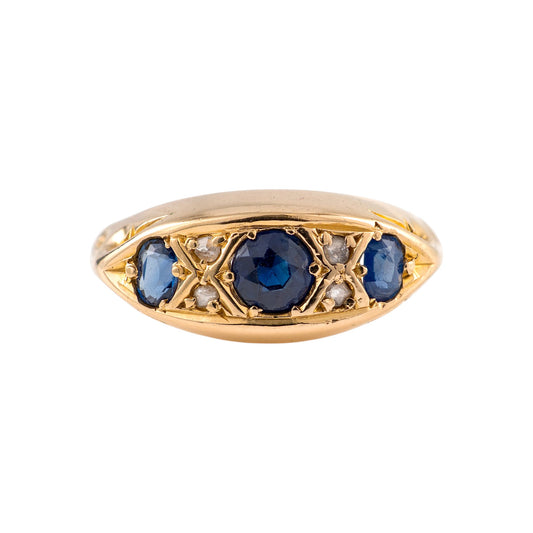 An antique sapphire ring featuring a central round blue sapphire flanked by smaller blue sapphires and tiny clear diamonds, set in an elongated marquise-shaped bezel on a white background.