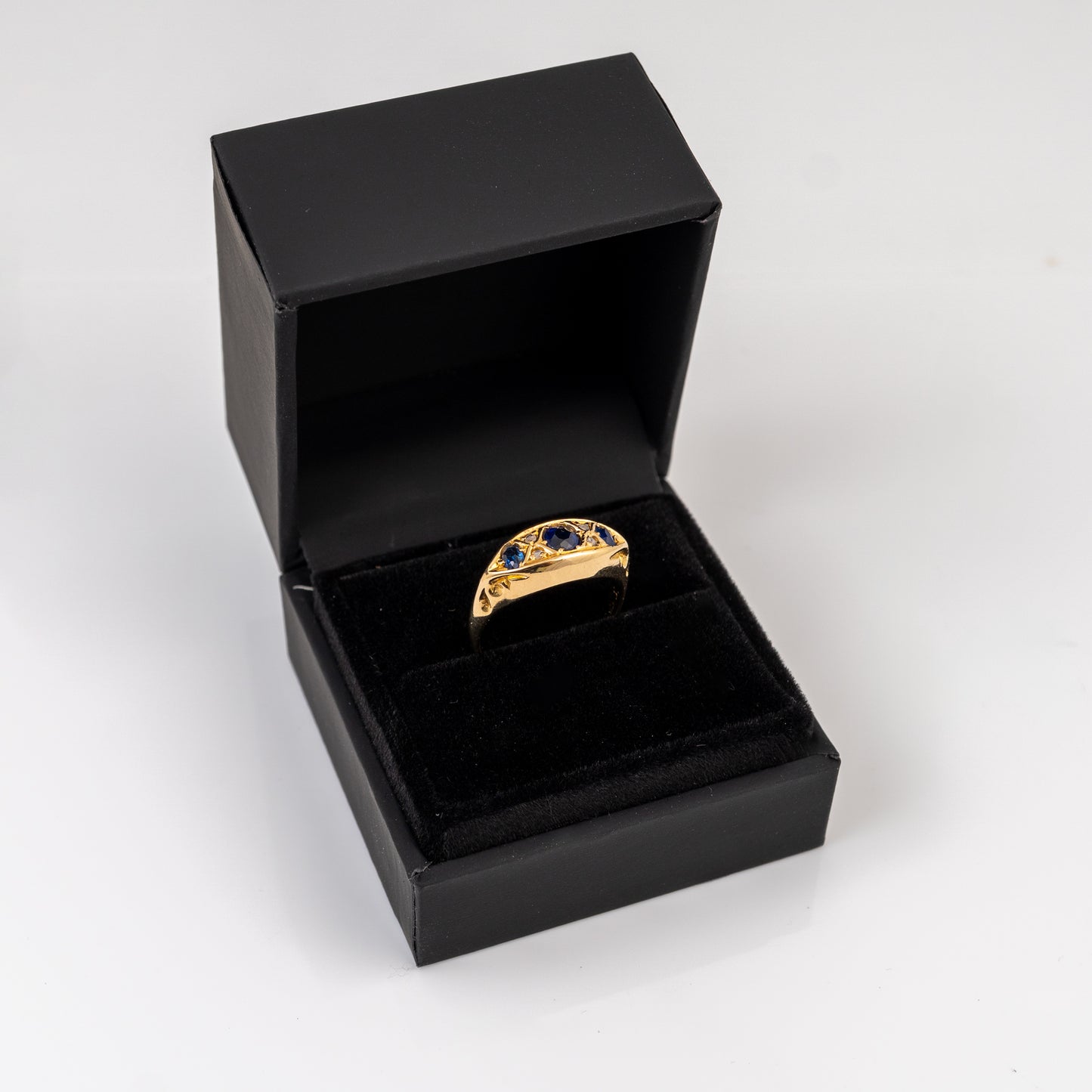 A gold signet ring with blue gemstone accents displayed inside an open black presentation box on a white background.