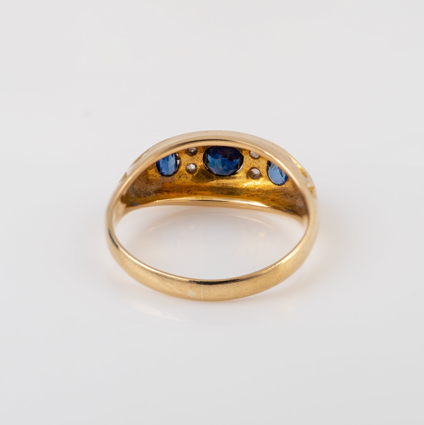 A vintage gold ring with a curved top set with blue sapphires and small clear stones, shown on a plain white background.
