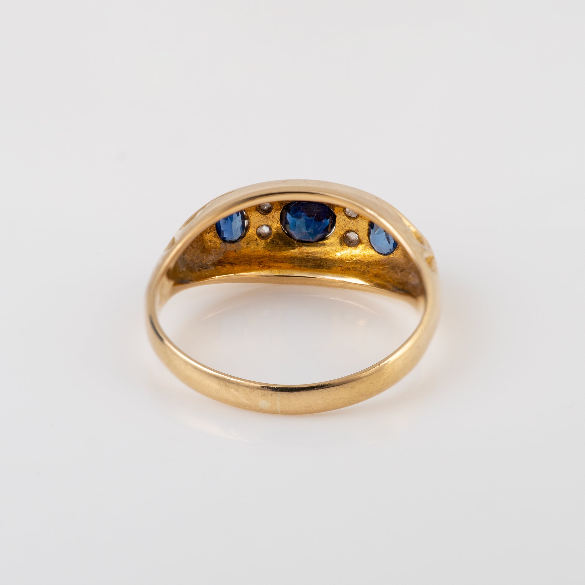 A vintage gold ring with a curved top set with blue sapphires and small clear stones, shown on a plain white background.