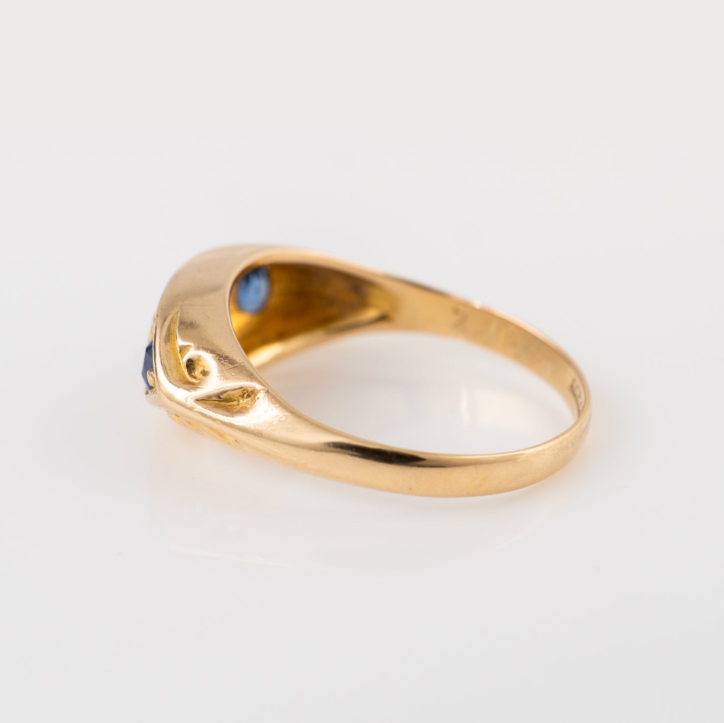 Antique sapphire gold ring with a curved, stylized setting featuring small round blue gemstones, photographed on a clean white background.