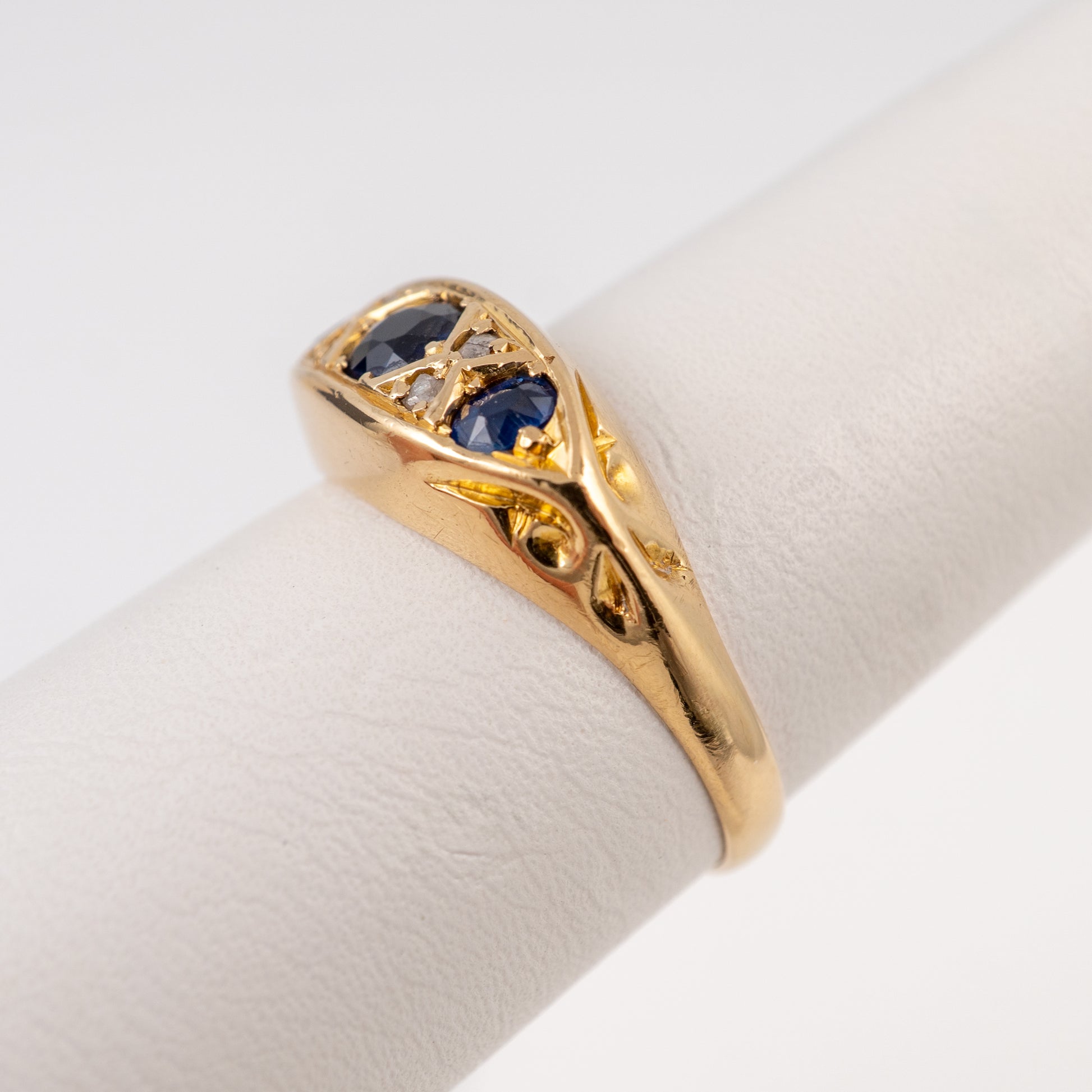 A gold ring with three blue gemstones, displayed on a white ring stand against a white background.