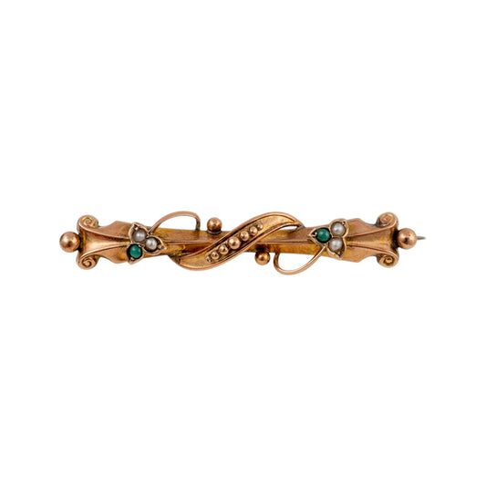 An ornate 19th-century gold brooch featuring a central twisted loop embellished with small green emeralds and white pearl-like accents, flanked by decorative scrollwork and bead details.
