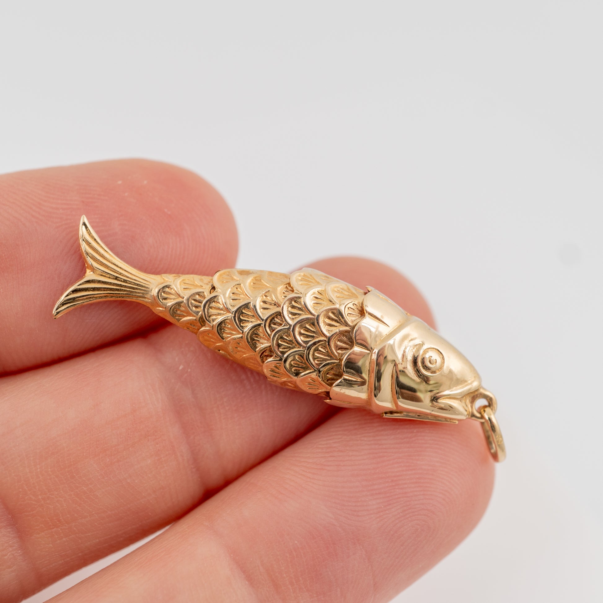 Articulated 9ct gold fish pendant shown in hand showing scale