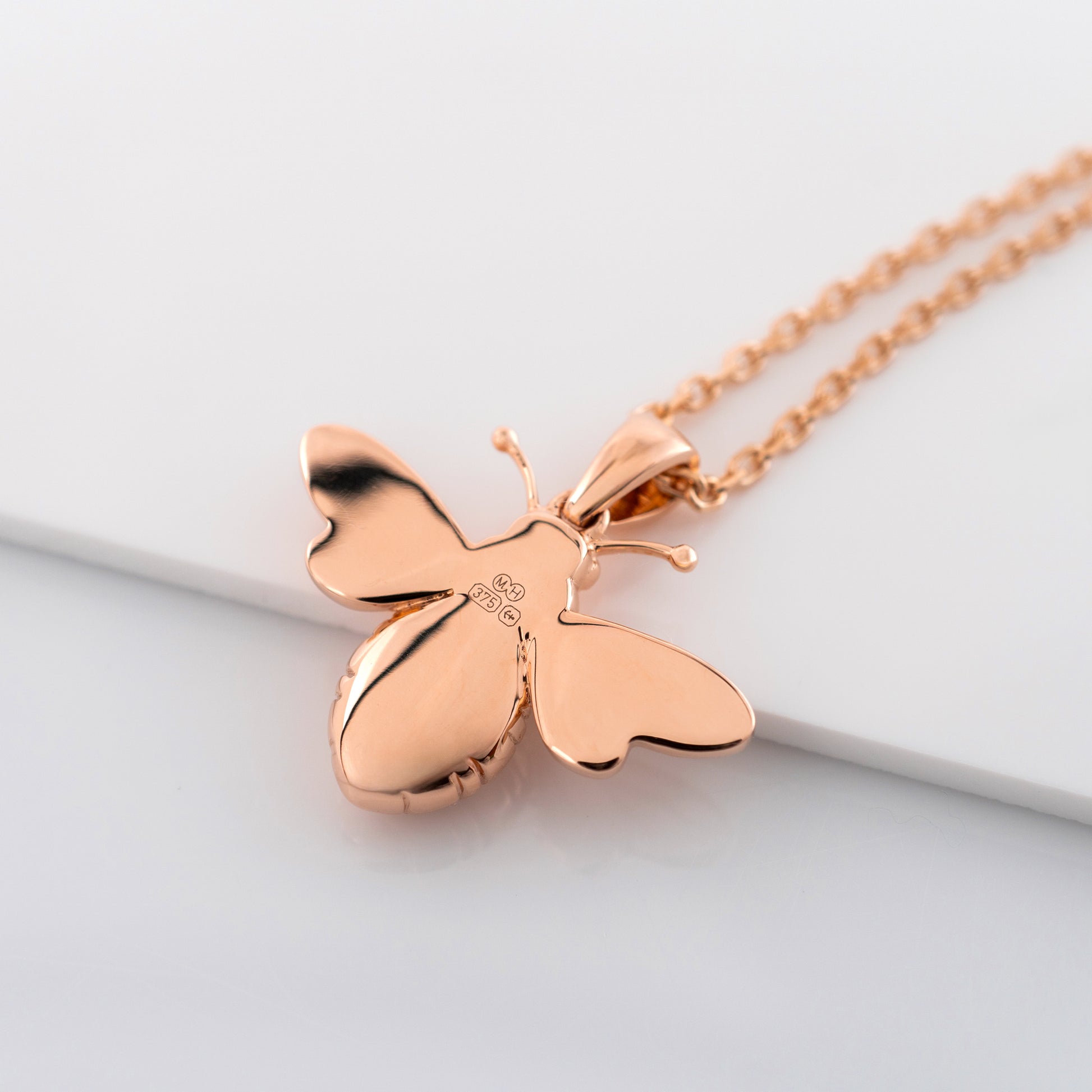 Rose gold butterfly necklace showing smooth reverse side and hallmarks on a light gray background