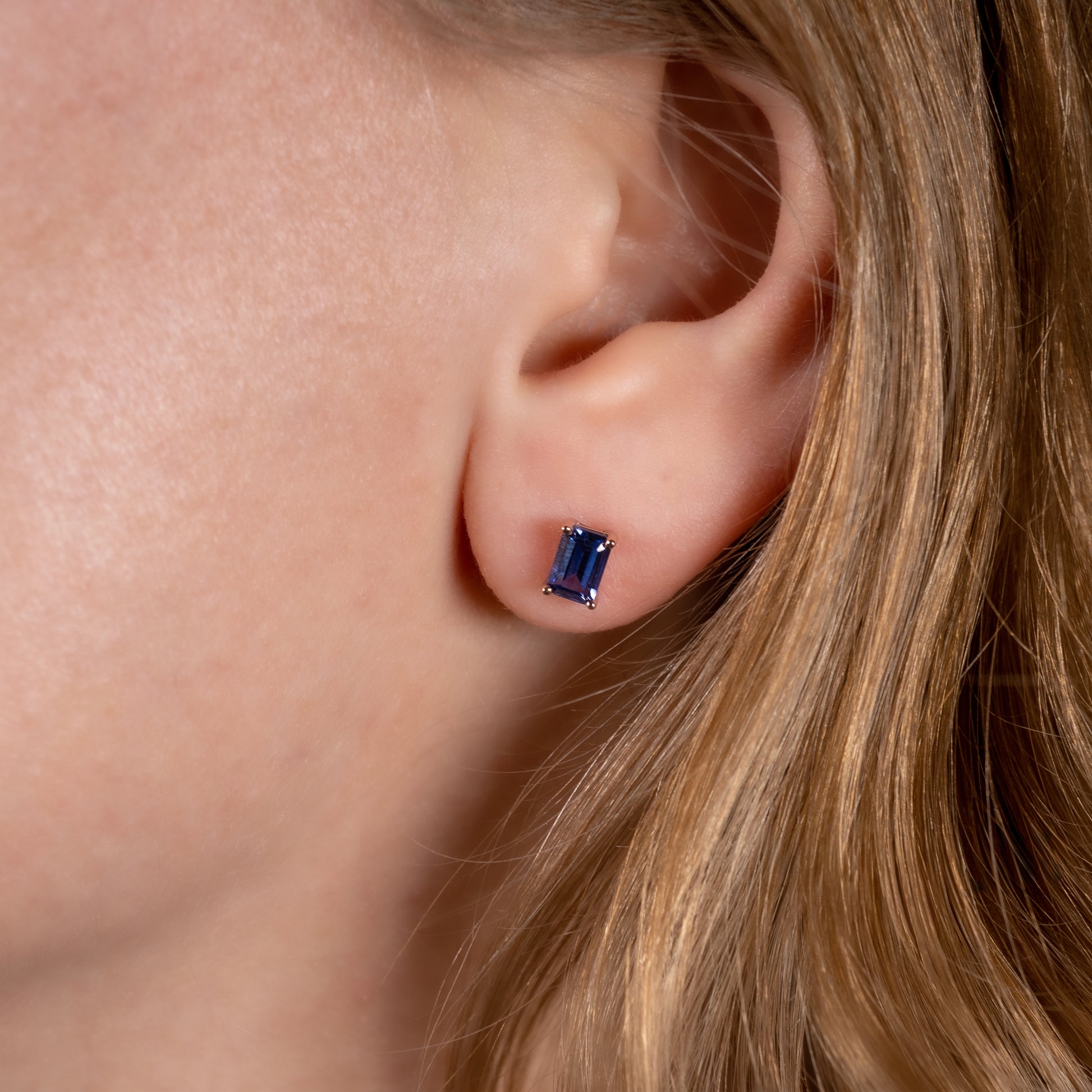 Close-up of an ear wearing a blue gemstone earring with blonde hair.