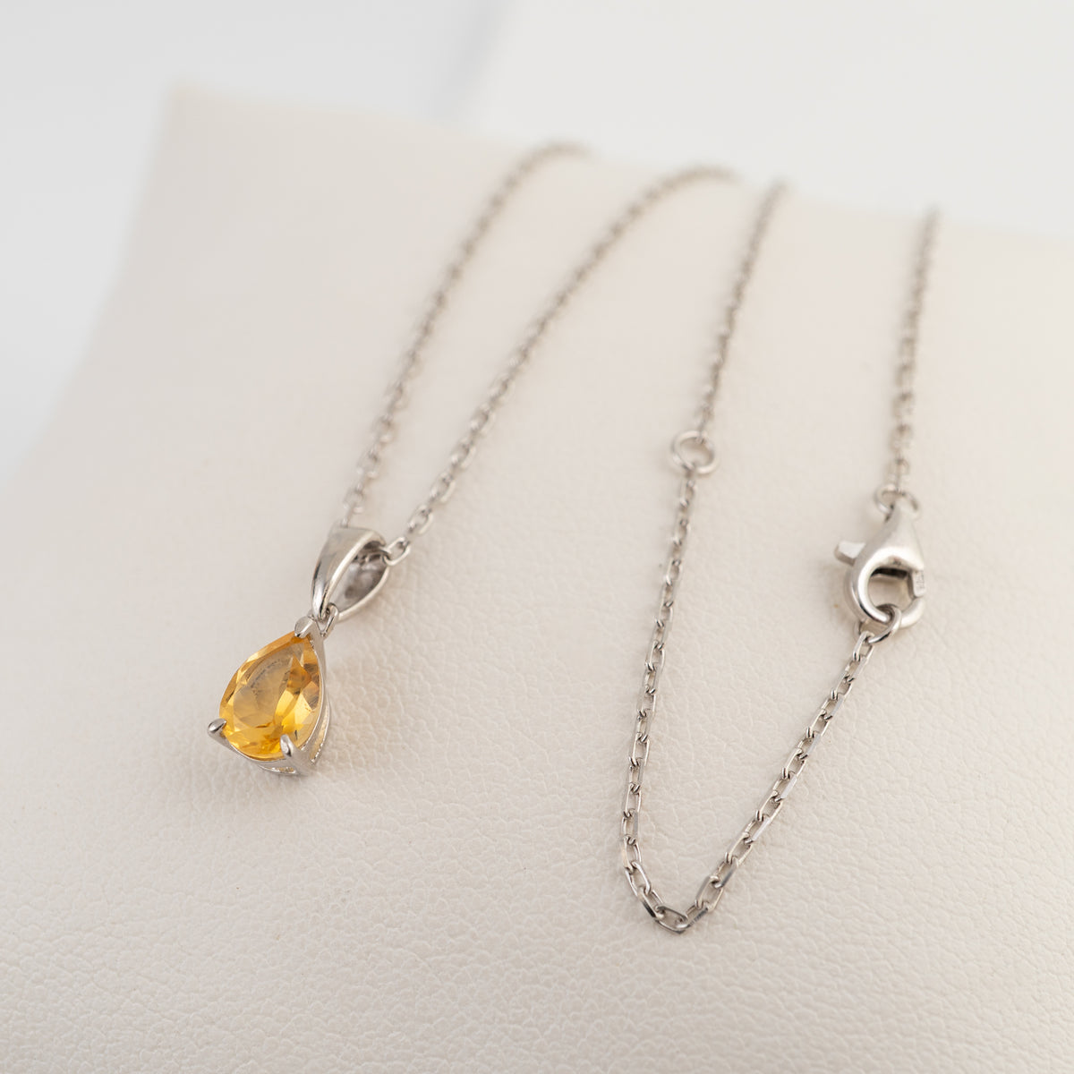 Citrine teardrop necklace laid out on a light cushion, showing the silver chain and clasp.