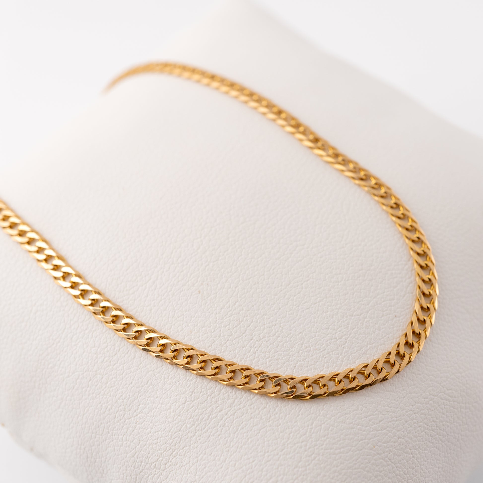 Close-up view of a 9ct gold curb chain necklace, showcasing the polished flat links on a white cushion