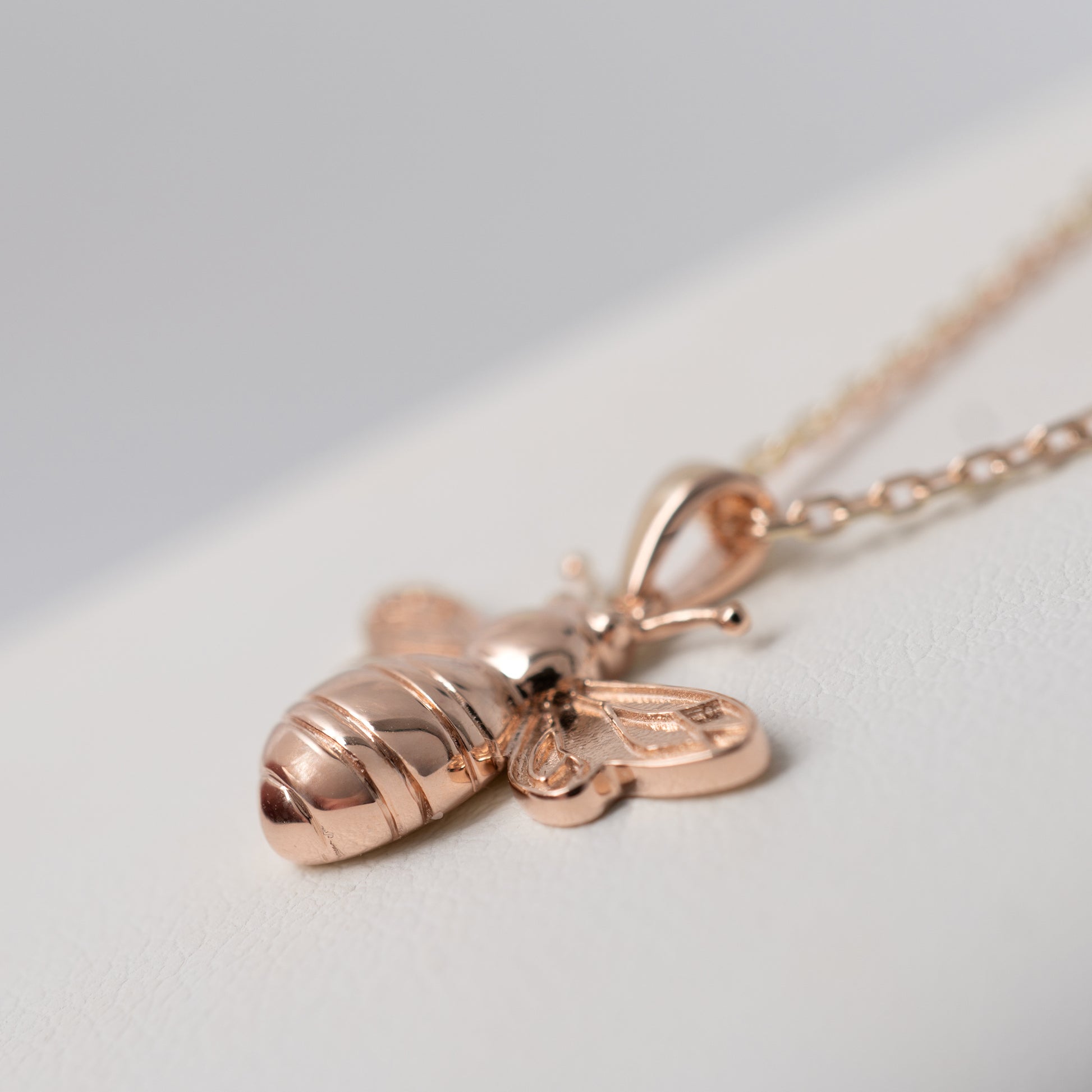 Rose gold bee necklace on a light gray background