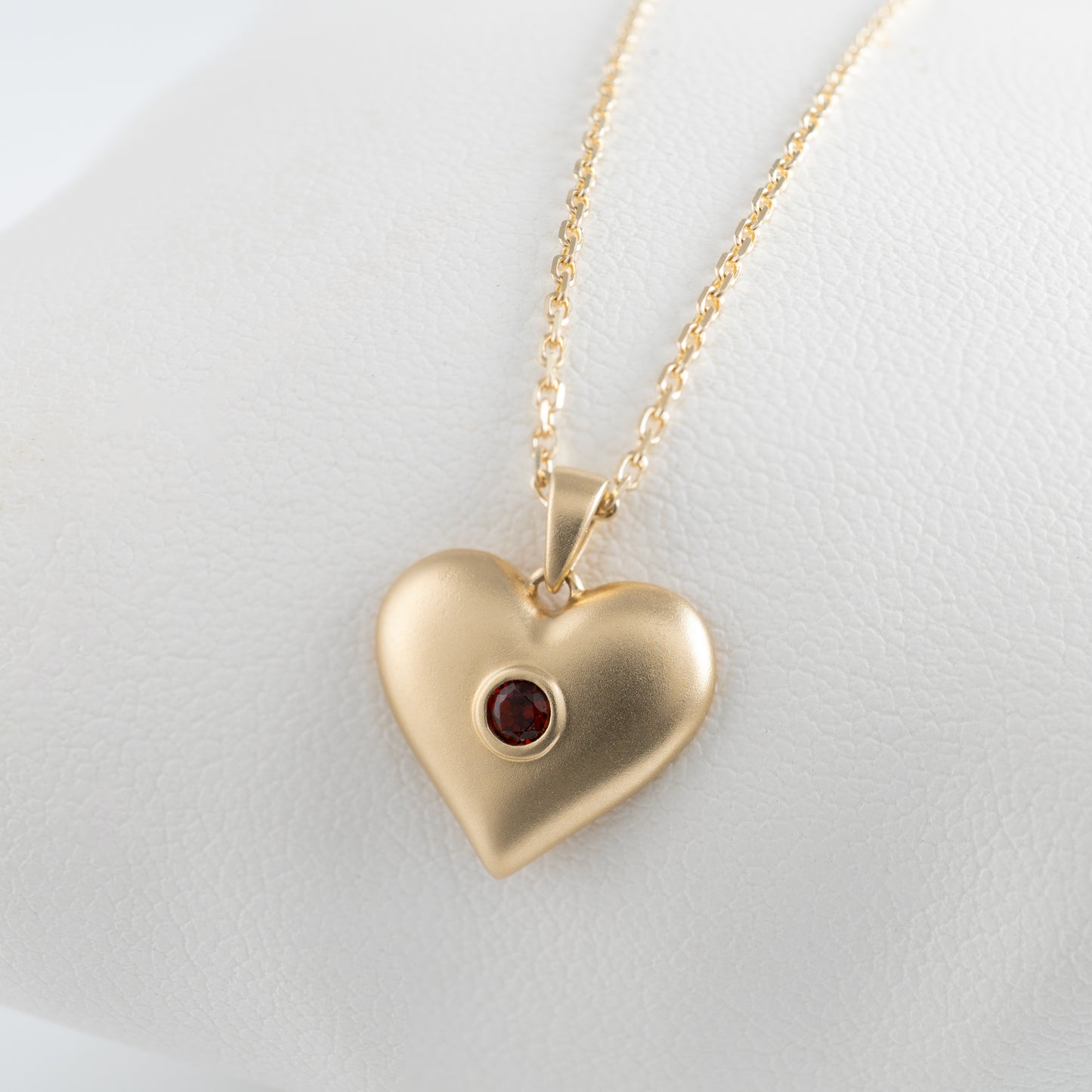 Close-up of matte gold heart pendant with garnet gemstone