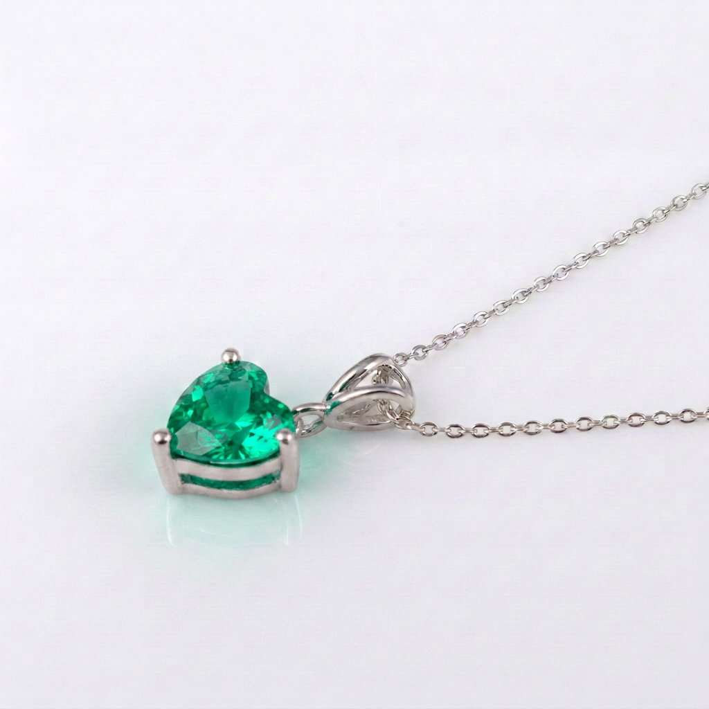 A silver heart-shaped pendant necklace featuring a vibrant green heart-cut gemstone, displayed on a clean white background.