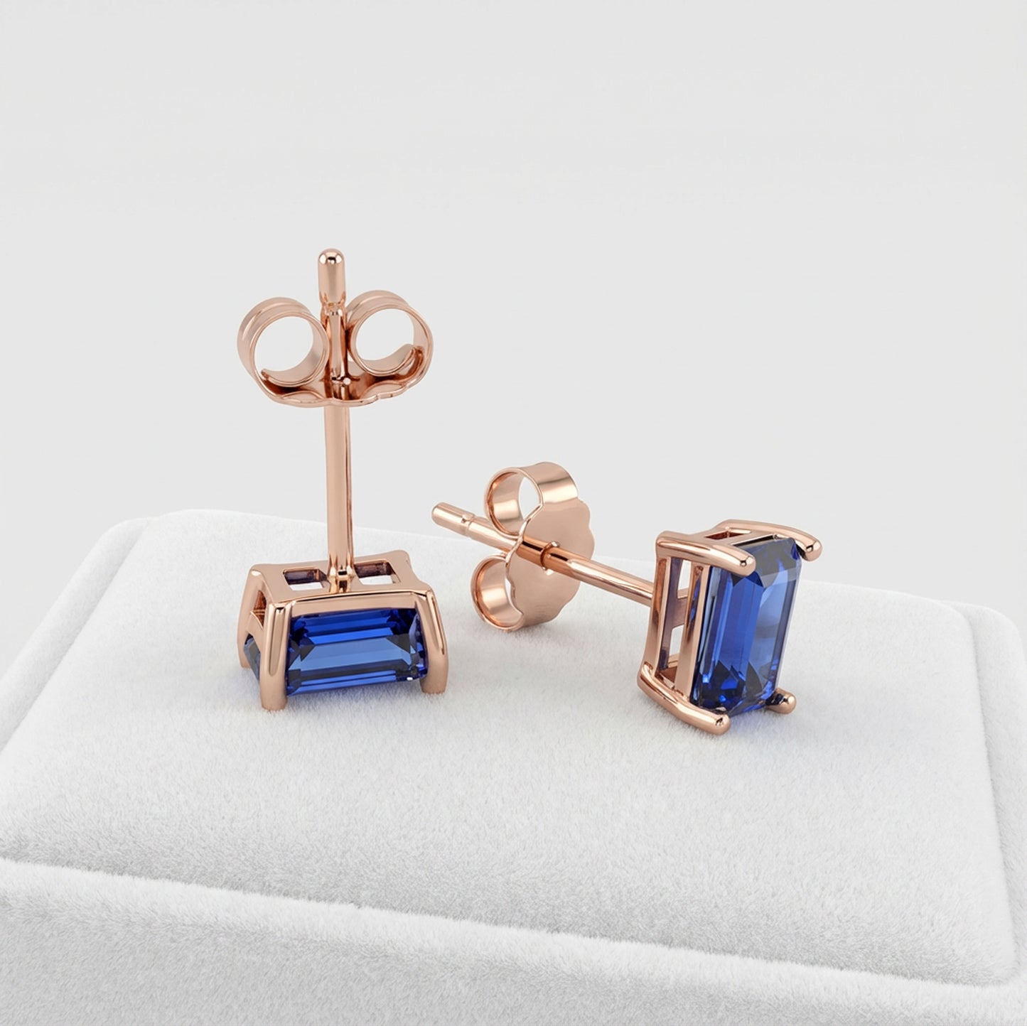 Rose gold earrings with blue lab sapphire gemstones on a white cushion