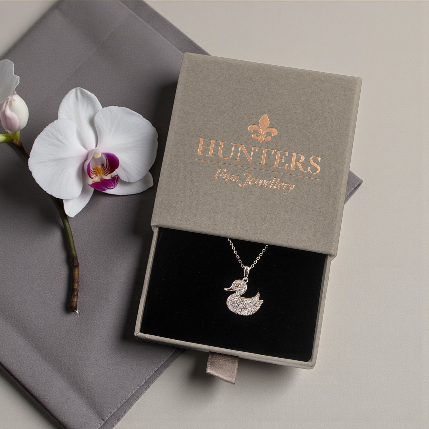 Jewelry box with a duck pendant and a white orchid on a gray surface