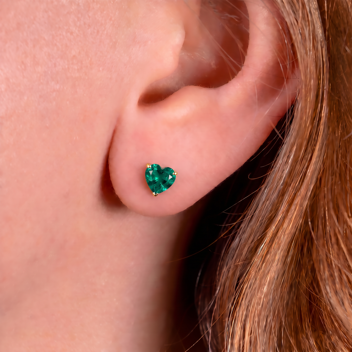Gold plated emerald heart stud earring worn on the ear, showing its petite 5mm size