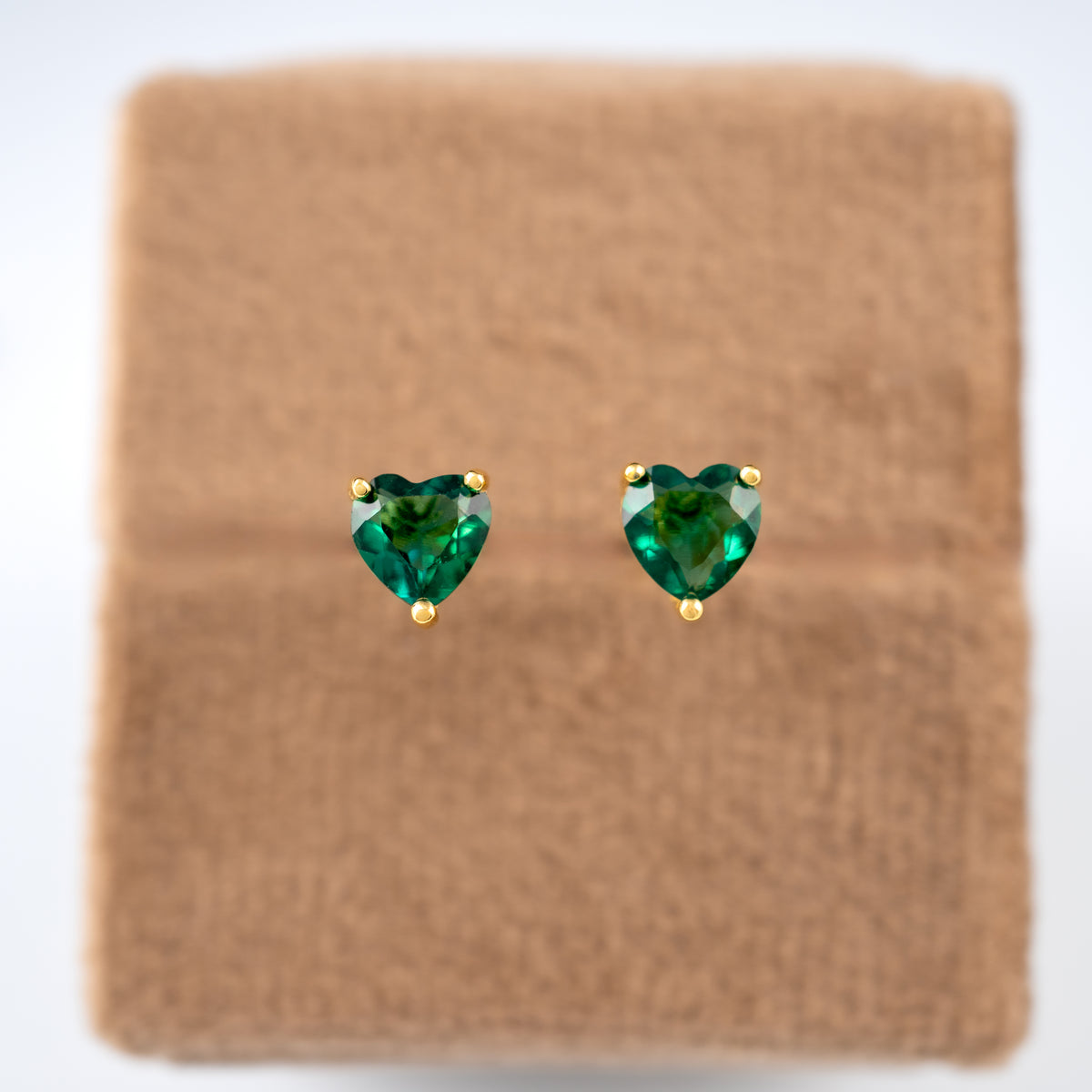 Heart-shaped green gemstone earrings on a brown display background