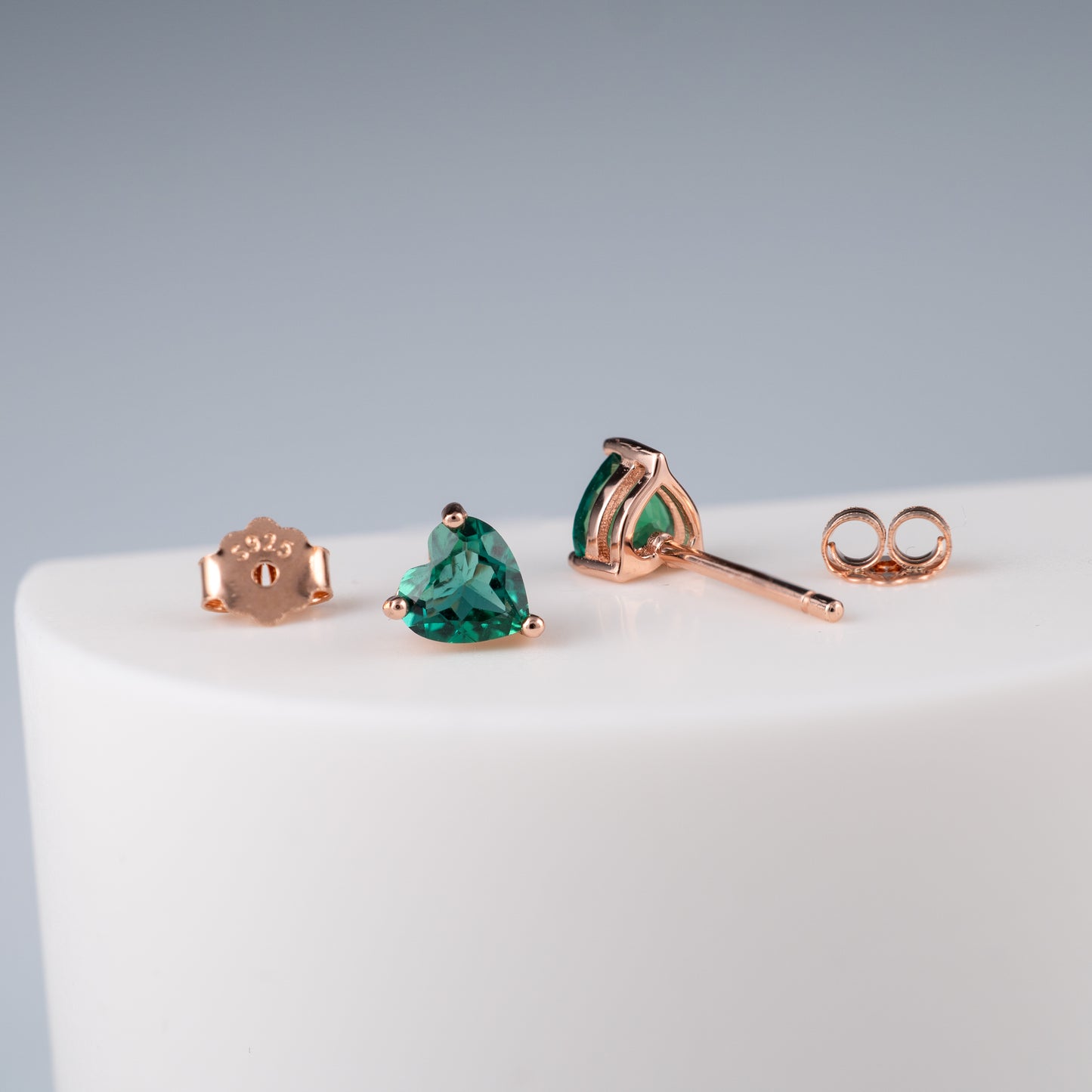 Rose gold emerald heart earrings with green gemstones on a white surface
