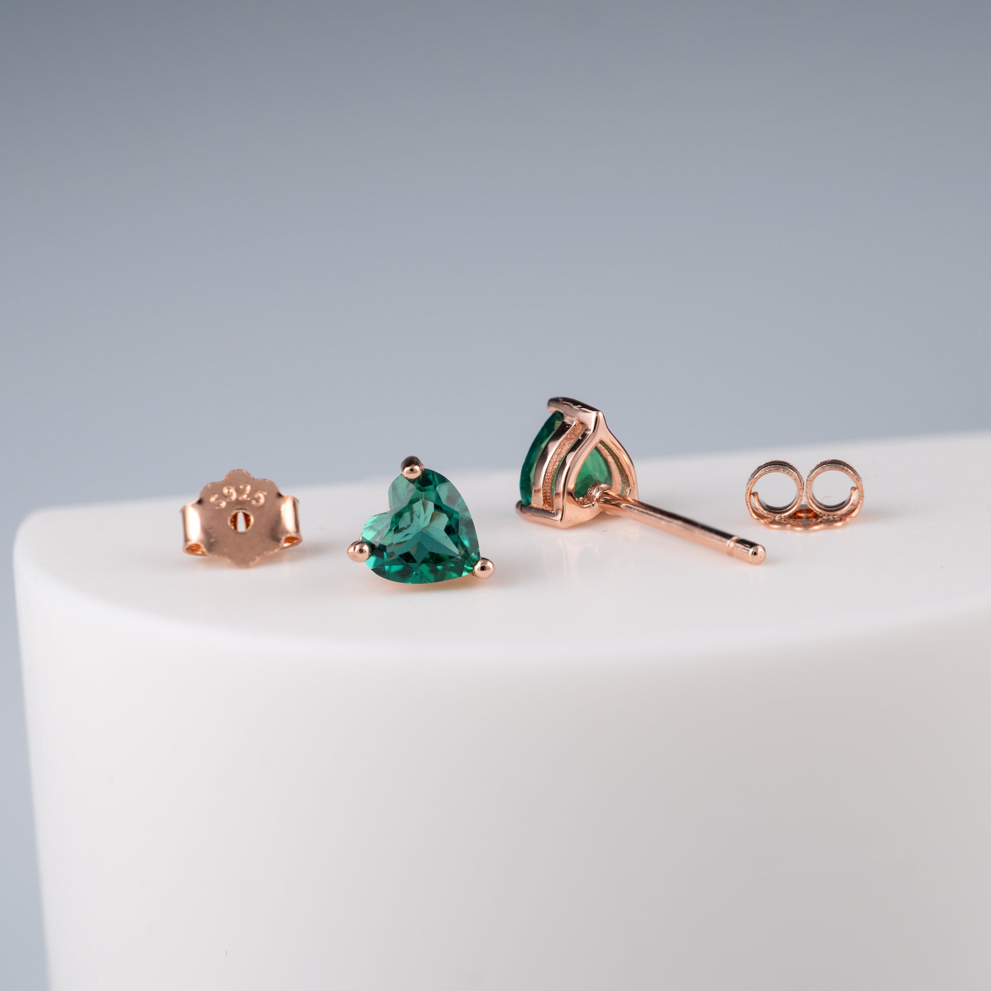 Rose gold emerald heart earrings with green gemstones on a white surface