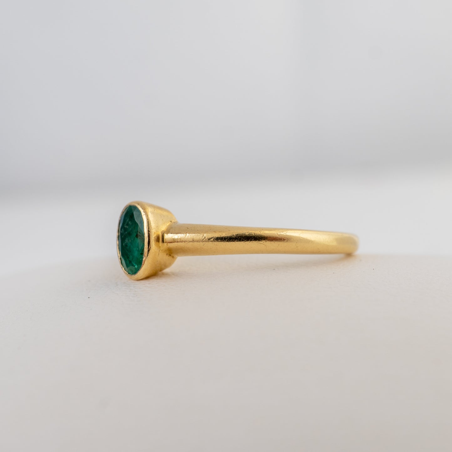 A gold ring with a bezel-set oval green gemstone, shown in profile against a clean, light gray background.