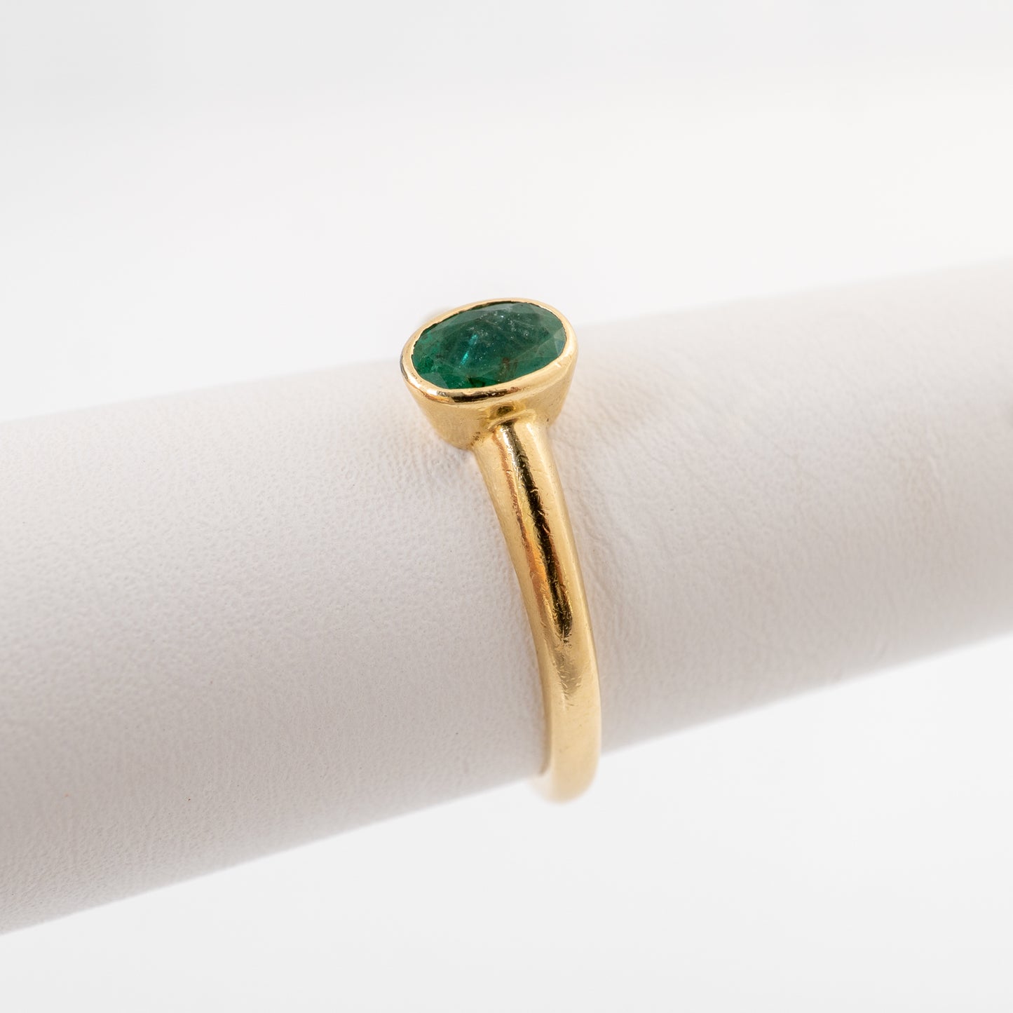 A gold ring with an oval emerald gemstone, displayed on a white ring stand against a white background.