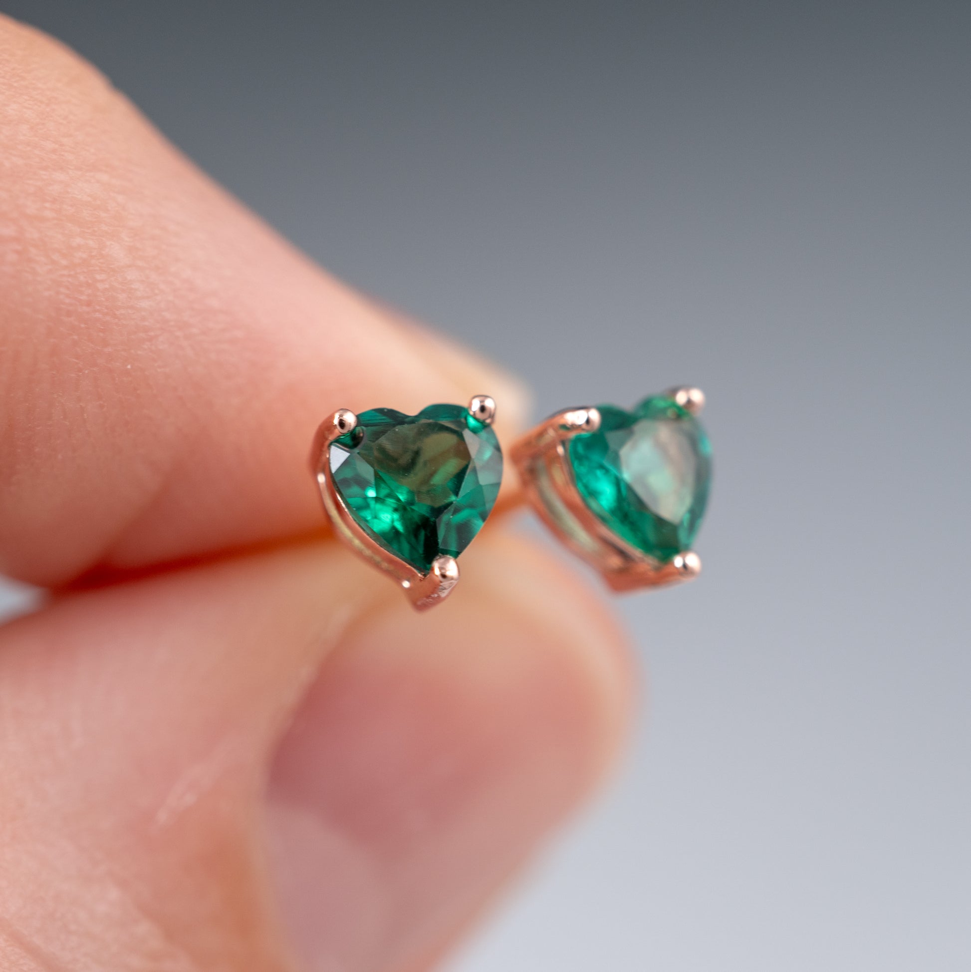 emerald heart earringsheld between fingers against a neutral background