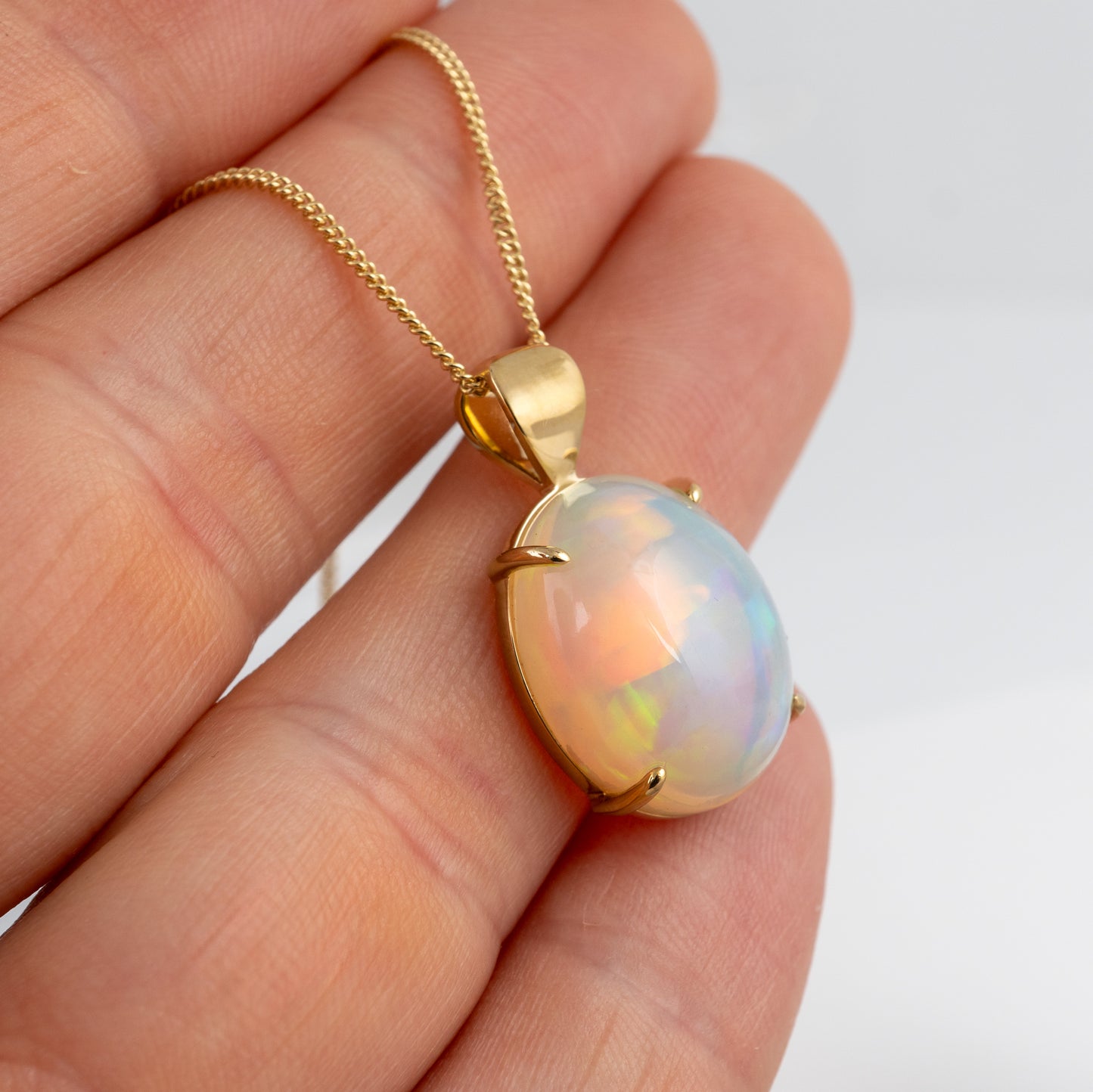 Opal pendant on a gold chain held in a hand against a white background
