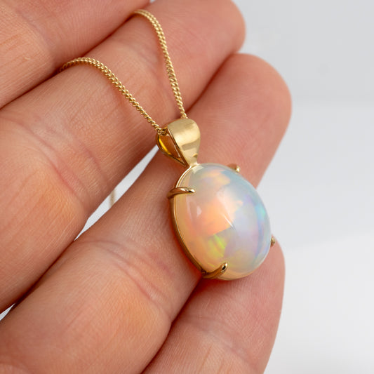 Opal pendant on a gold chain held in a hand against a white background