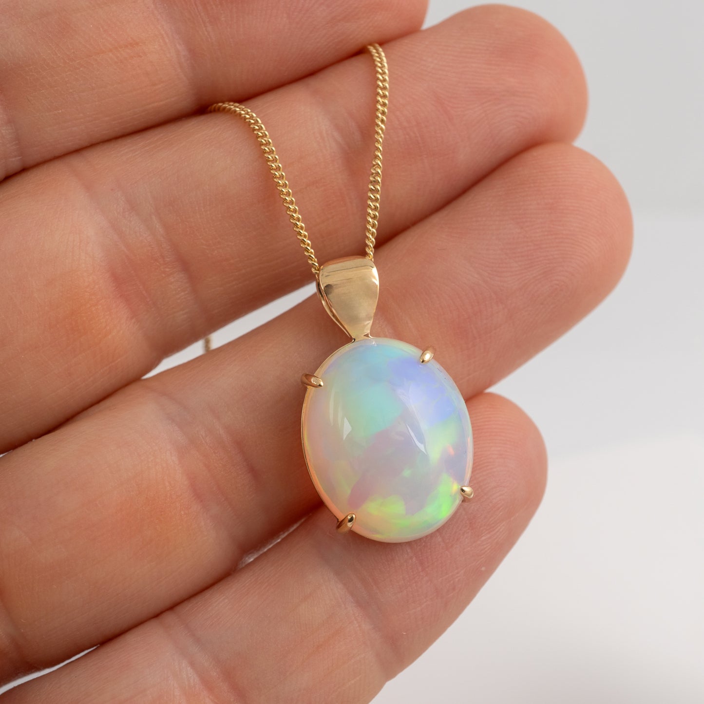 Opal pendant on a gold chain held in a hand against a white background