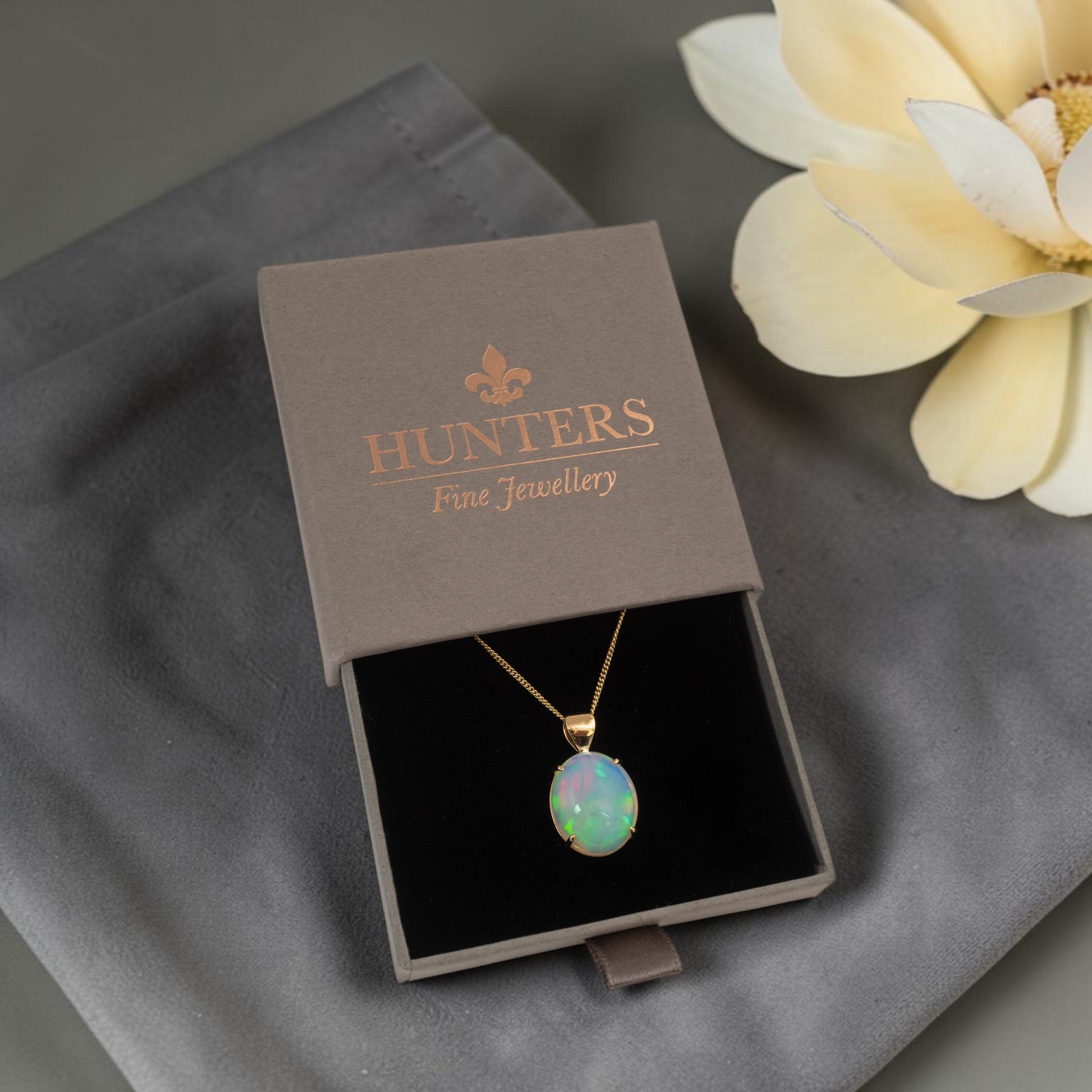 Opal pendant necklace in a Hunters Fine Jewellery box on a gray surface with a flower.
