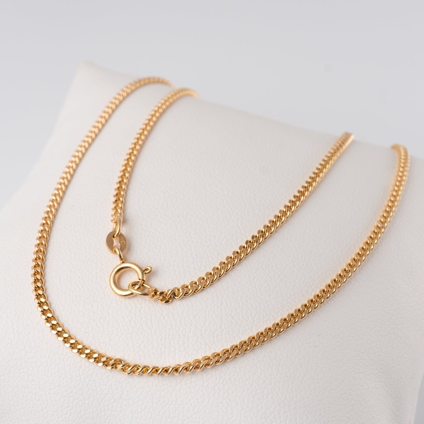 9ct gold flat curb link necklace displayed on white stand, showing spring ring clasp