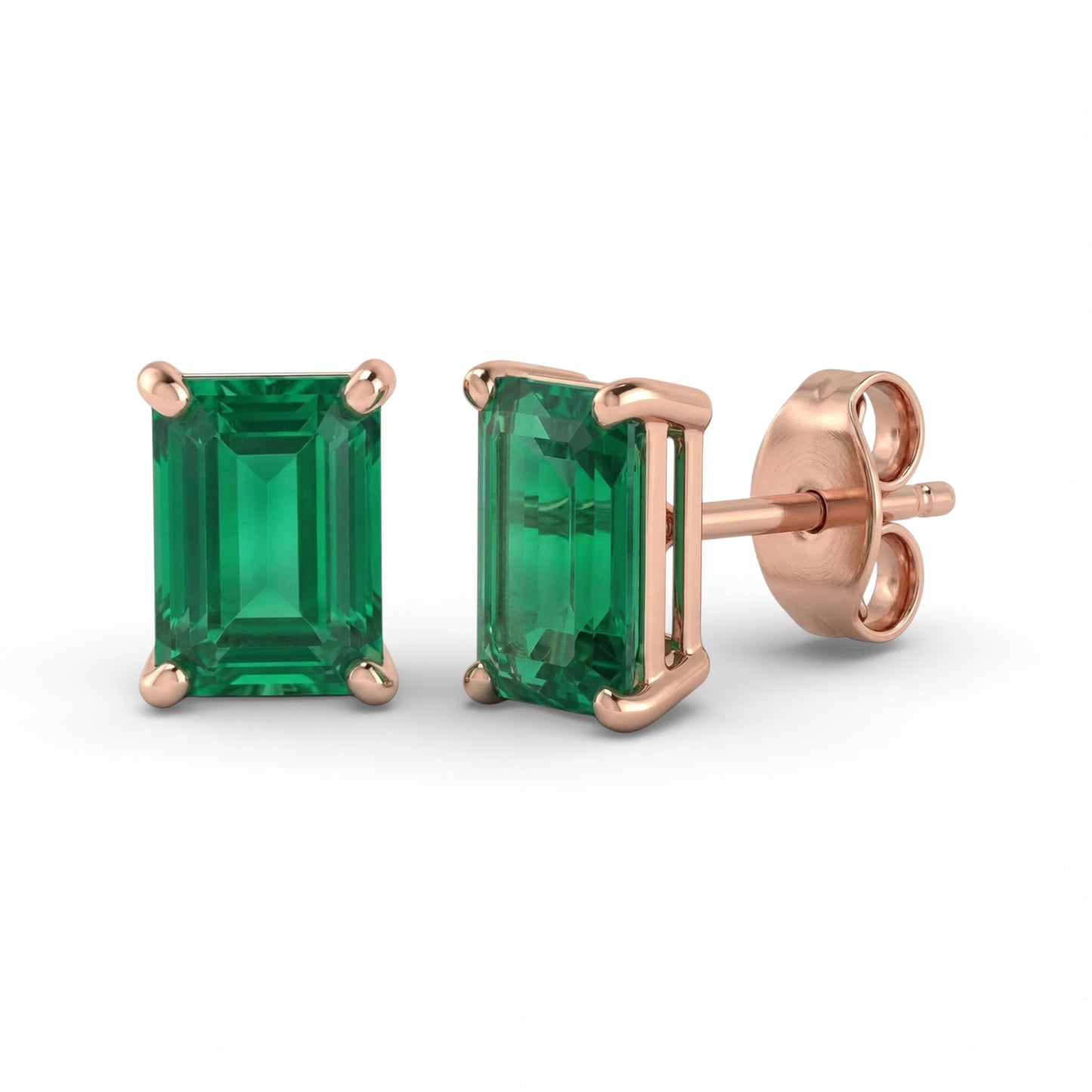 Pair of lab emerald earrings with rose gold settings on a white background