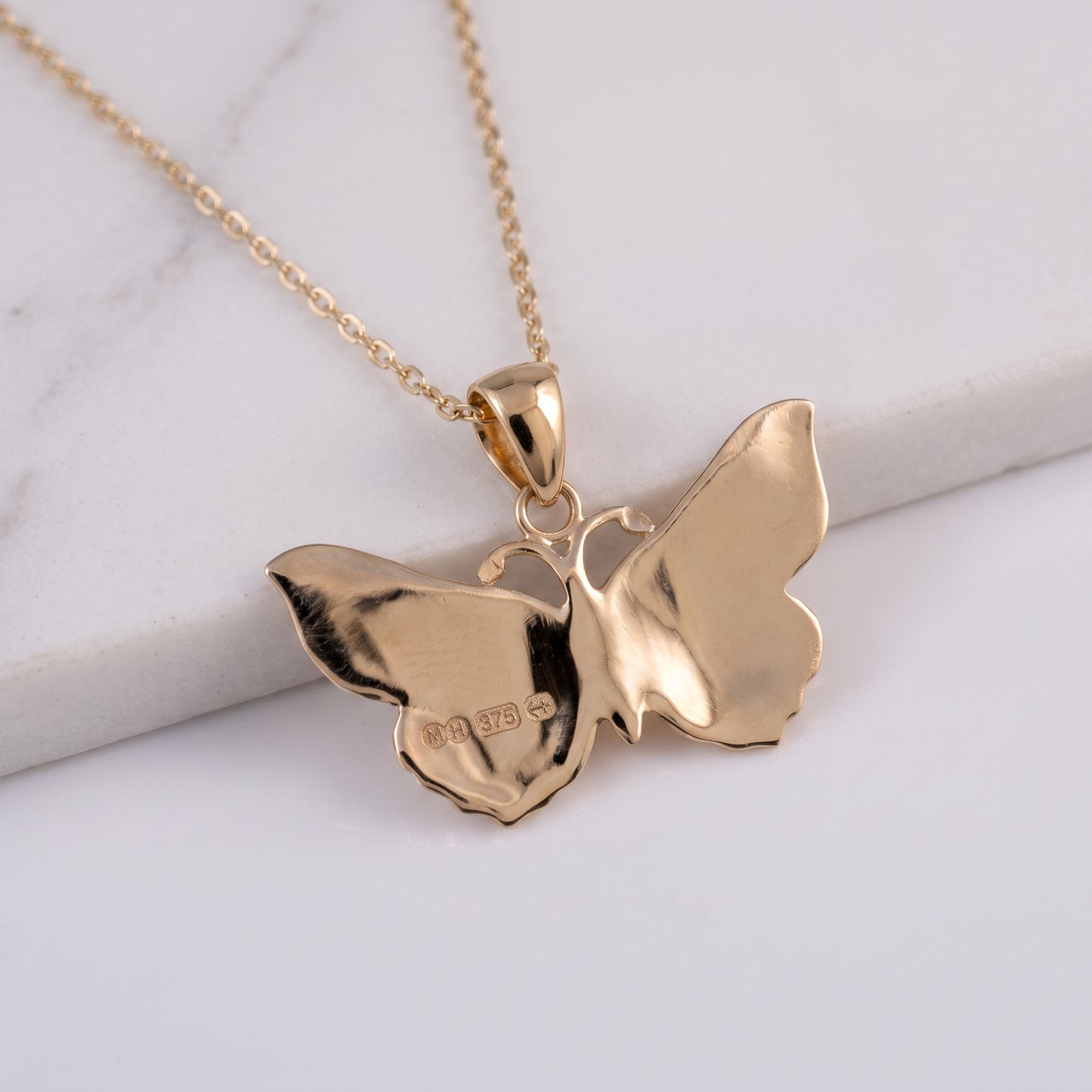 A gold butterfly pendant necklace on a delicate gold chain, displayed on a white marble slab against a white background.