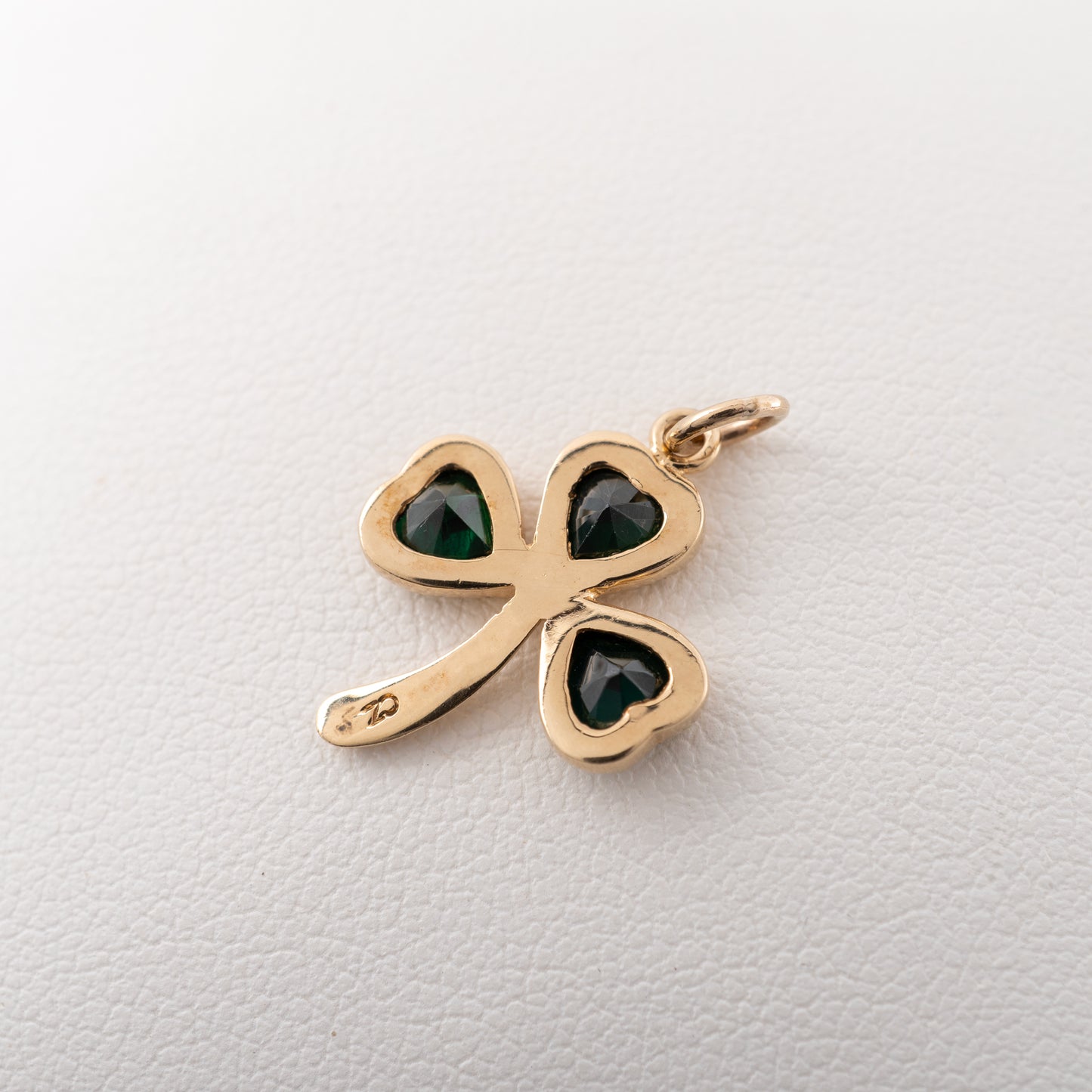 Gold shamrock necklace featuring dark green gemstones, showing reverse side flat on a light background