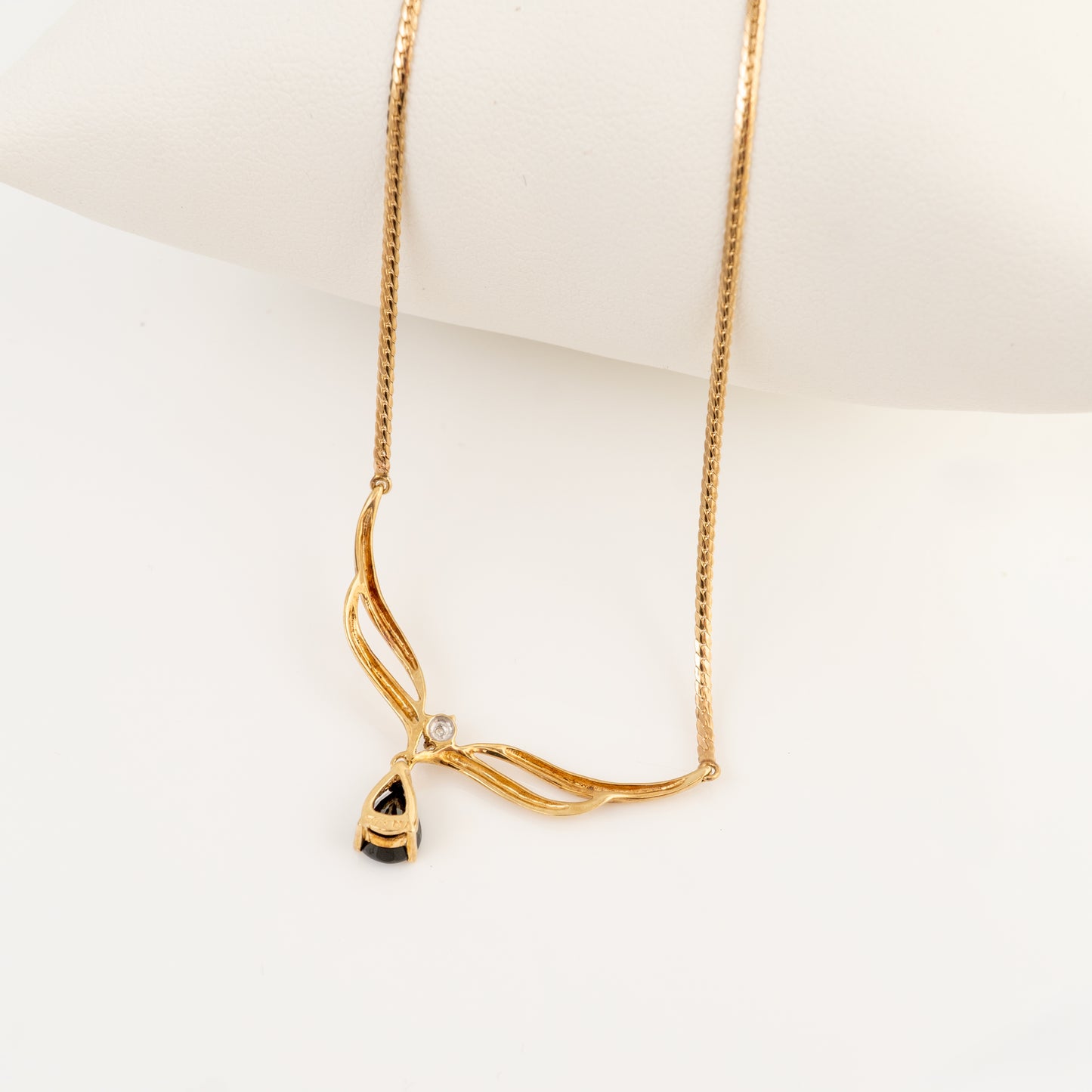 A gold necklace with a twisted, wave-like pendant design and a small clear stone, displayed on a white mannequin bust against a white background.