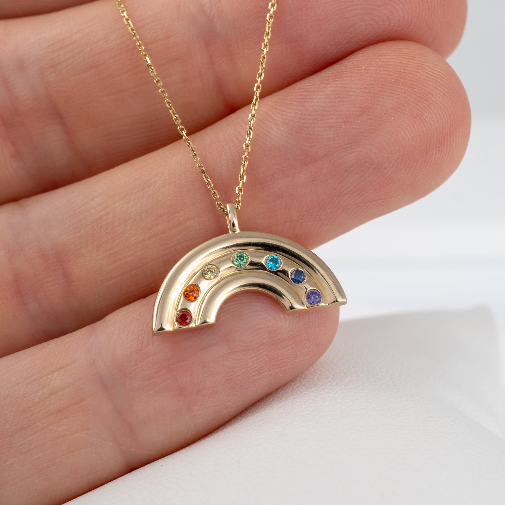 gold rainbow necklace in persons hand