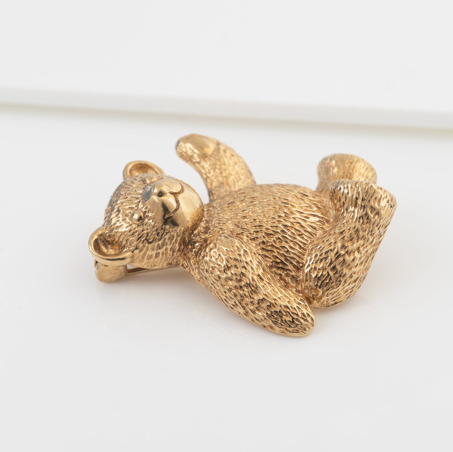 A gold teddy bearvbrooch, photographed on a clean white background.