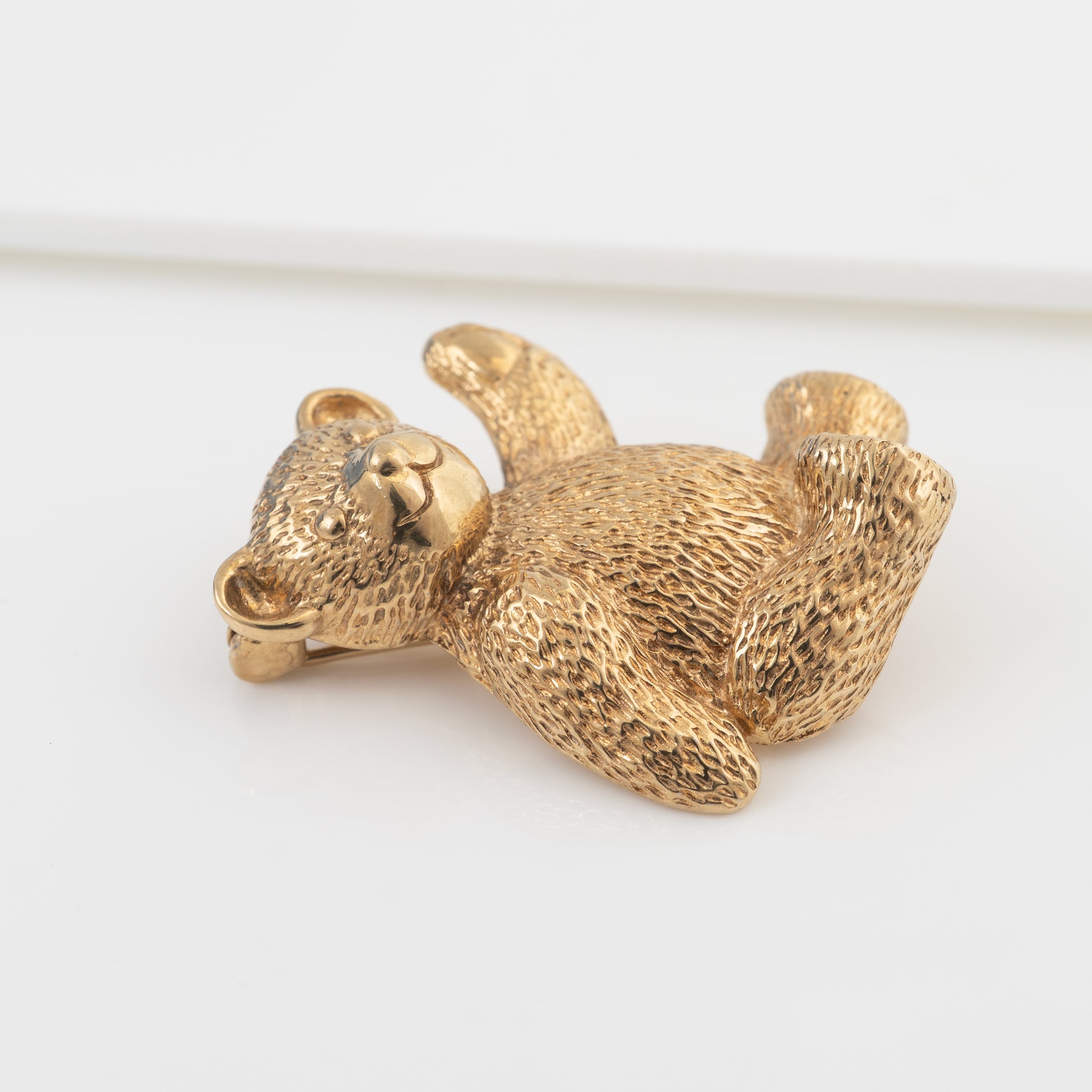 A gold teddy bearvbrooch, photographed on a clean white background.