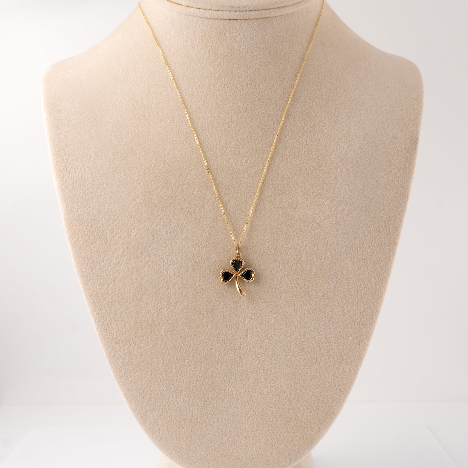 Gold shamrock pendant with green stones displayed on a bust, illustrating the necklace’s scale