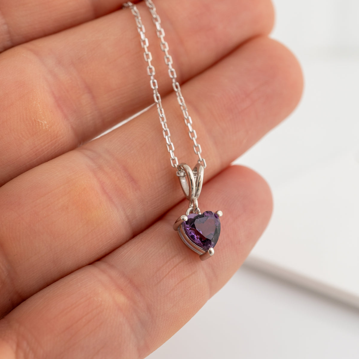 hand holding amethyst heart necklace to show the colour against the skin