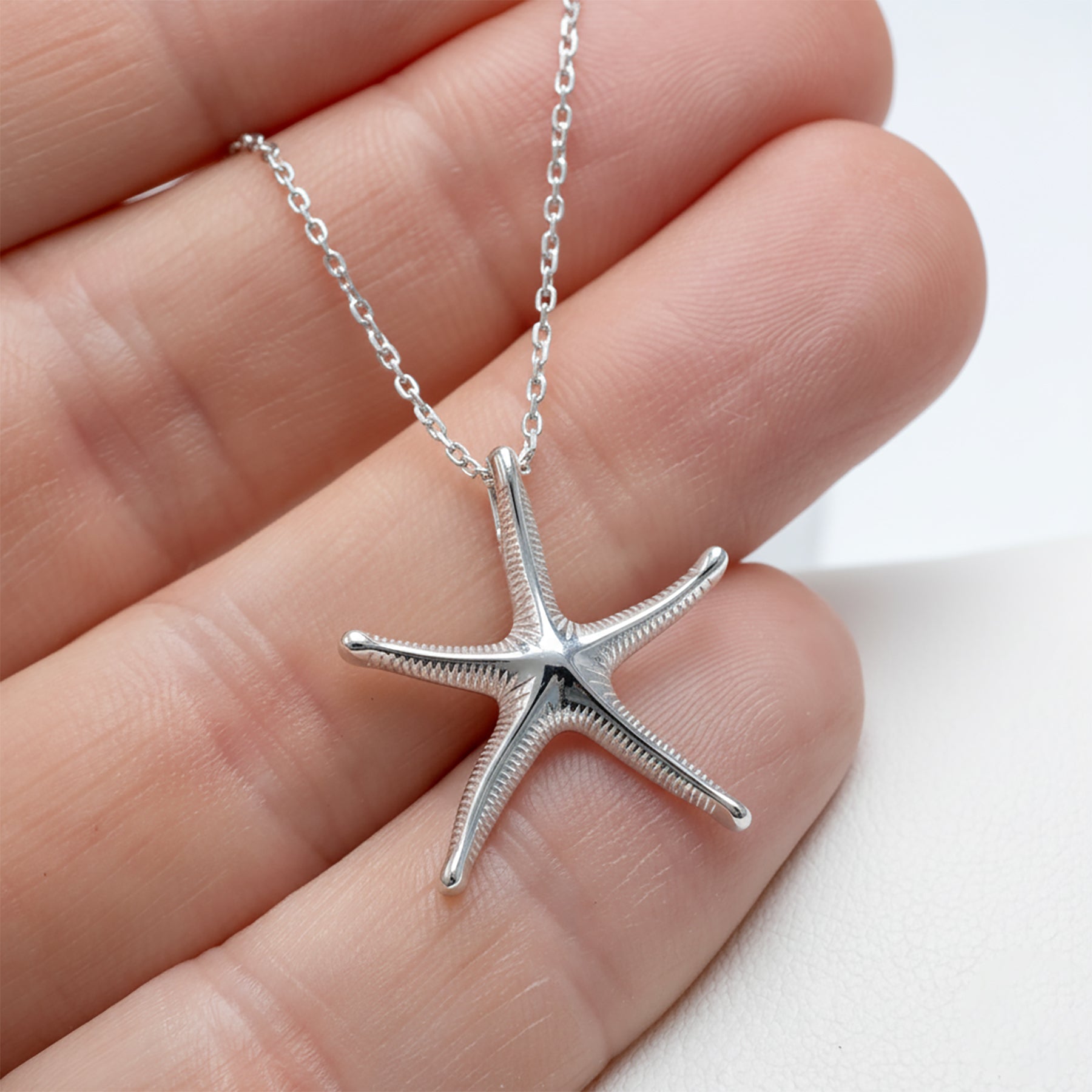 Silver starfish pendant on a chain held between fingers