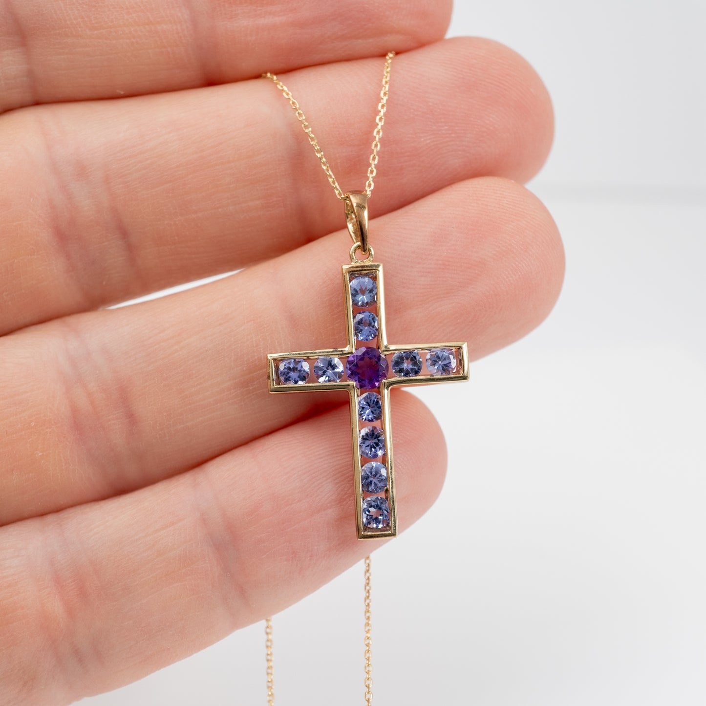 hand holding gemstone set gold crucifix necklace