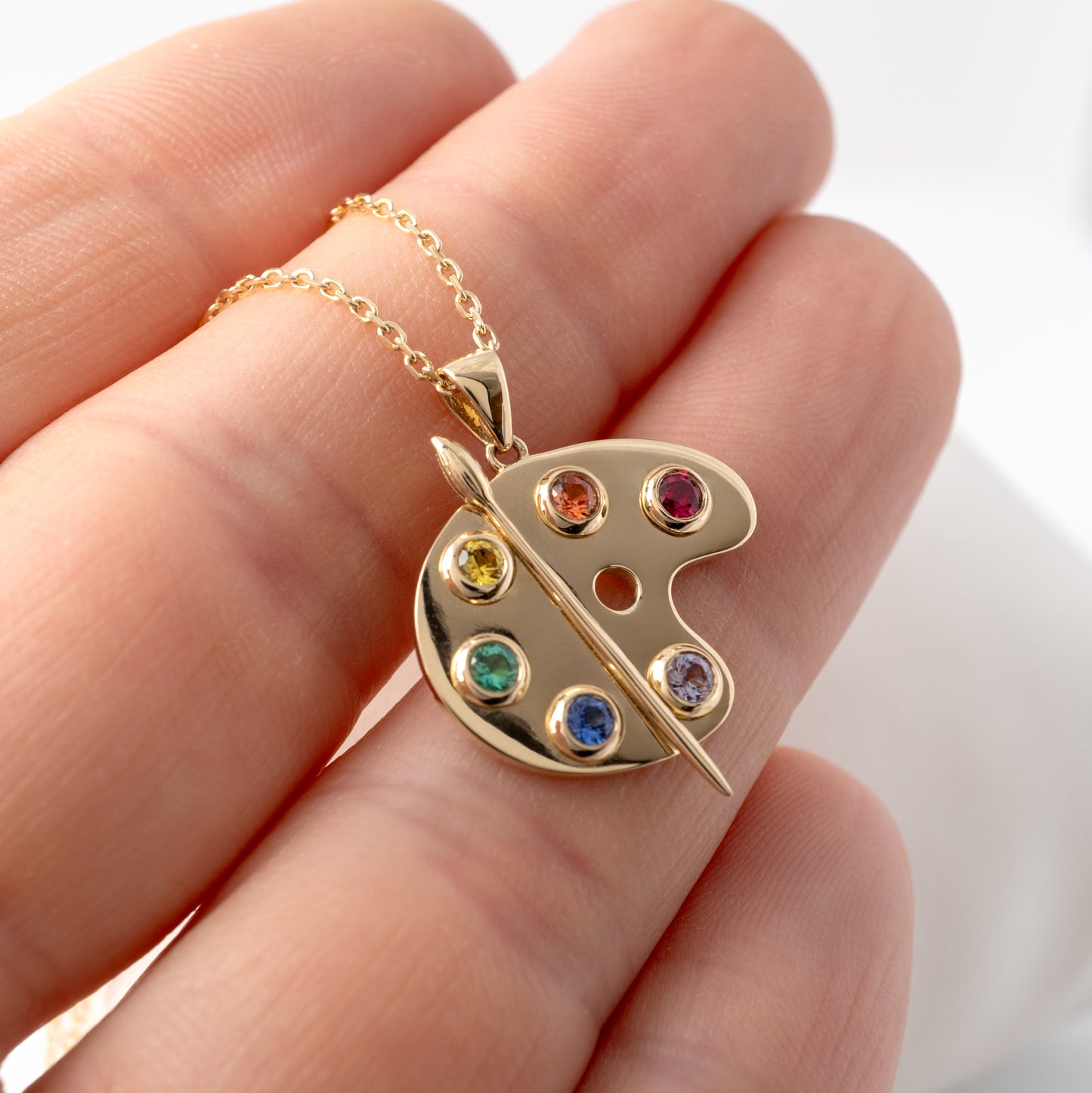 holding a Unique gold artist palette necklace with colourful lab-grown gemstones