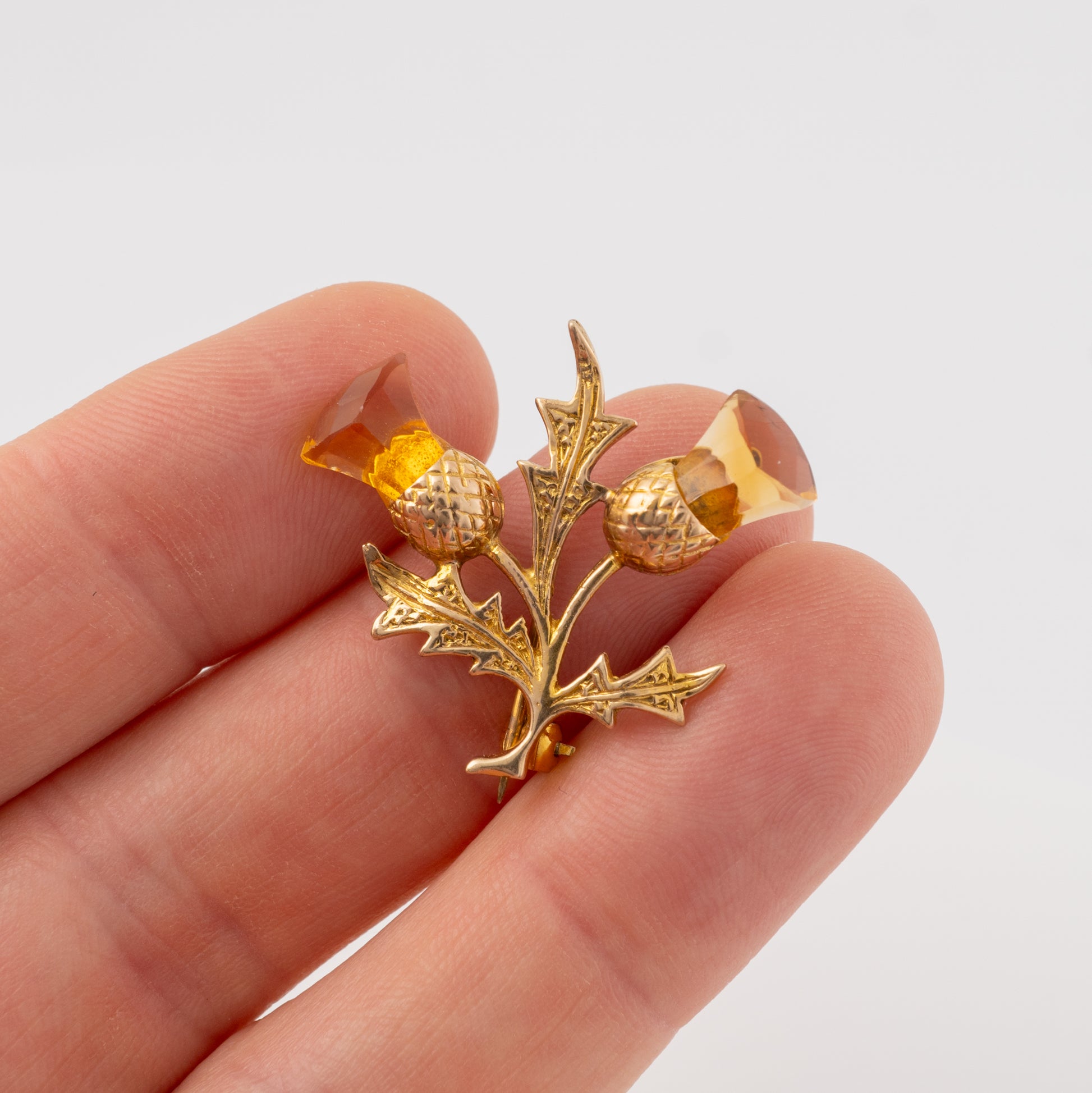 Holding a gold thistle brooch with citrine gemstones to show its size and scale