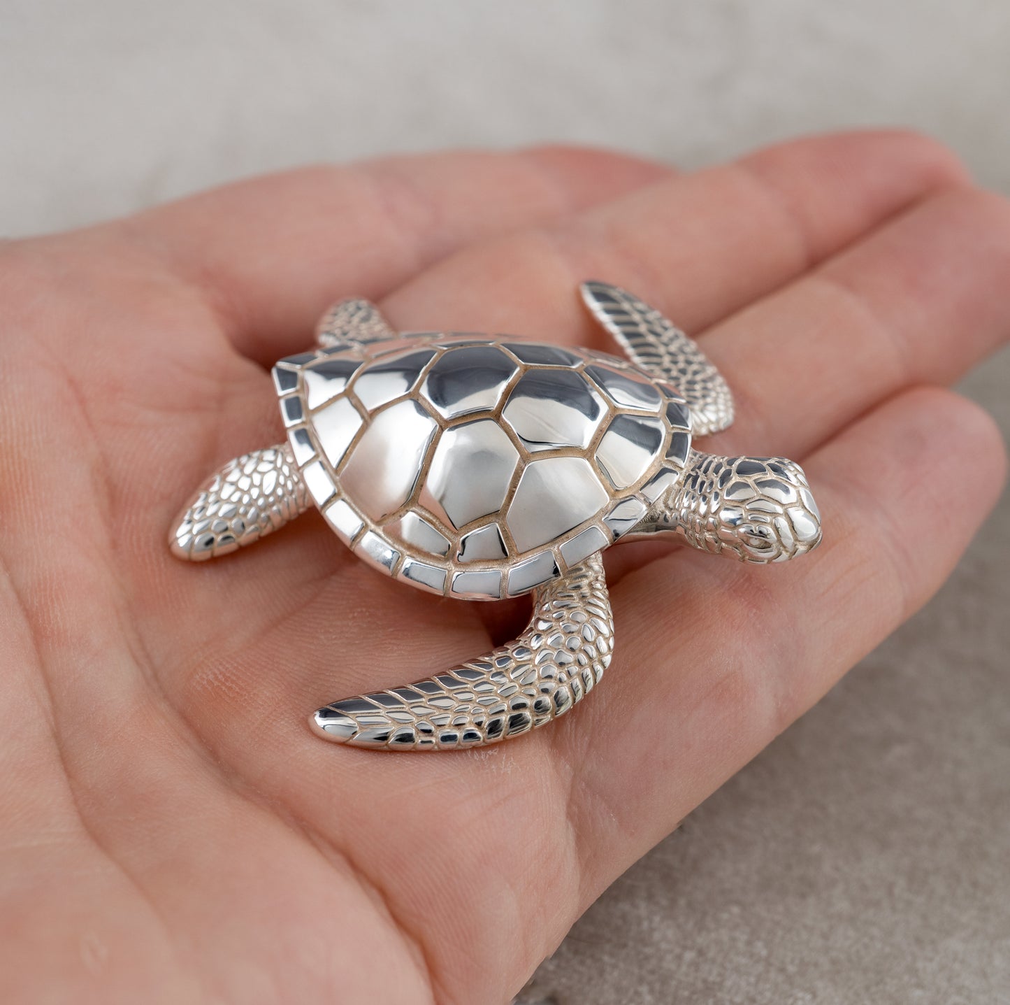 Silver sea turtle figuringe held in a hand against a neutral background