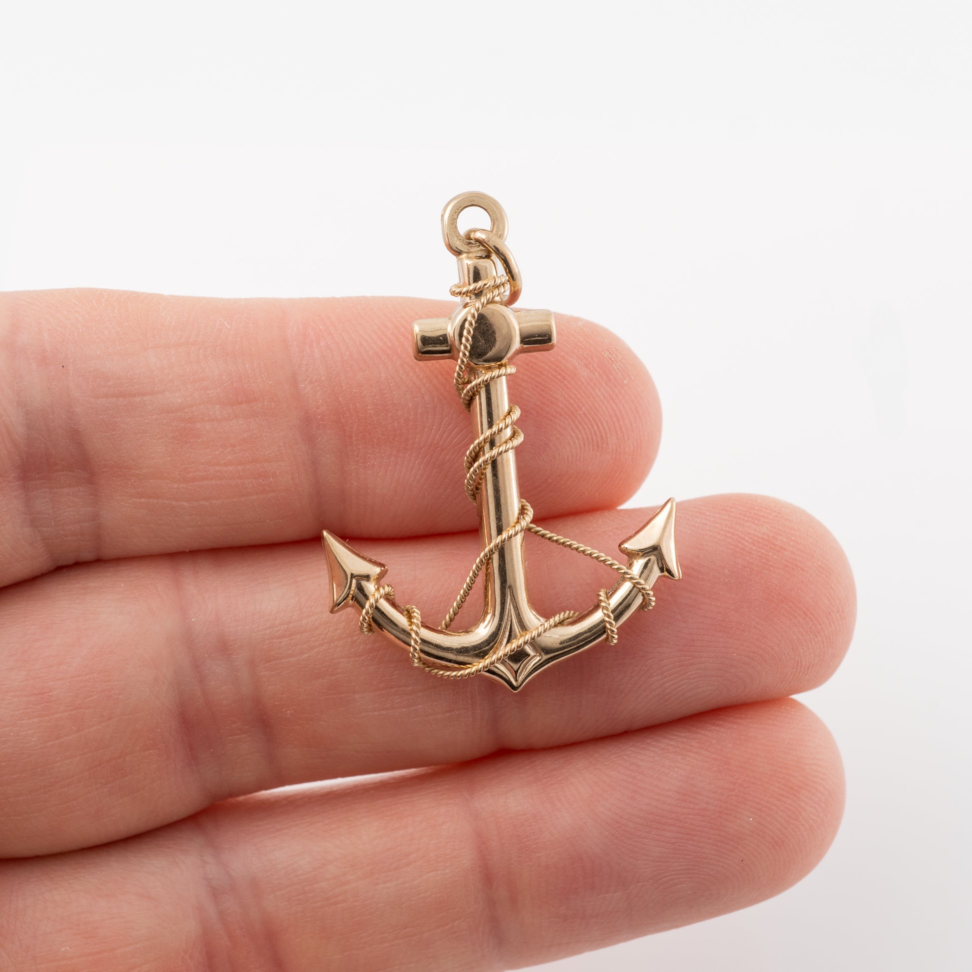 Gold anchor pendant held in hand to display scale and craftsmanship