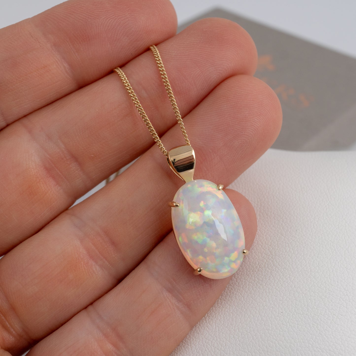 Gold necklace with an opal pendant held between fingers on a white background
