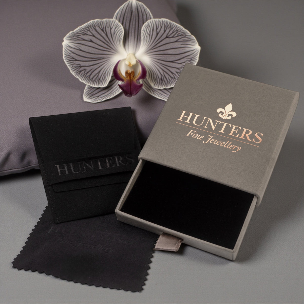 Hunters Fine Jewellery branded gift box with a black cloth and orchid on a grey background