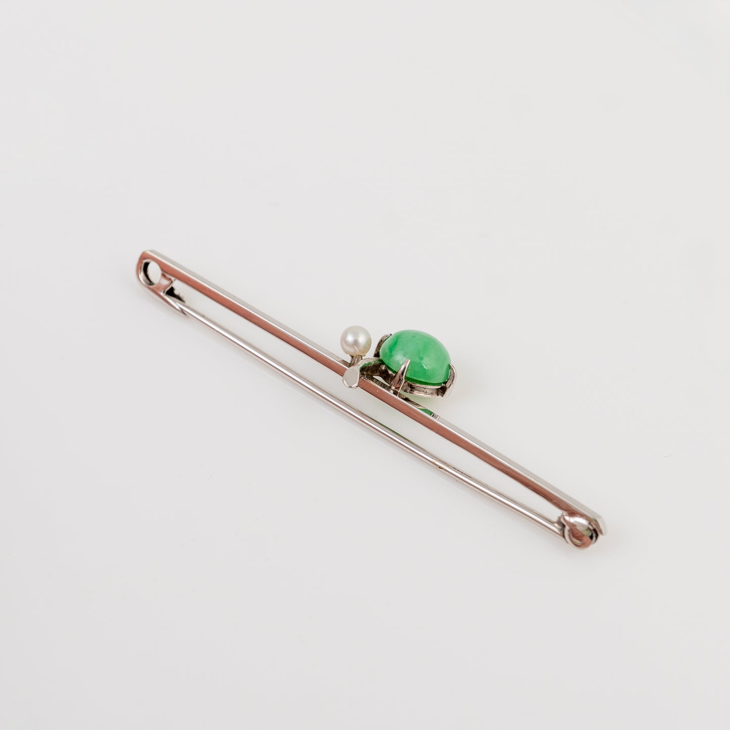 A silver-toned bar pin featuring a polished green oval hade cabochon and a small white pearl, displayed on a clean white background.