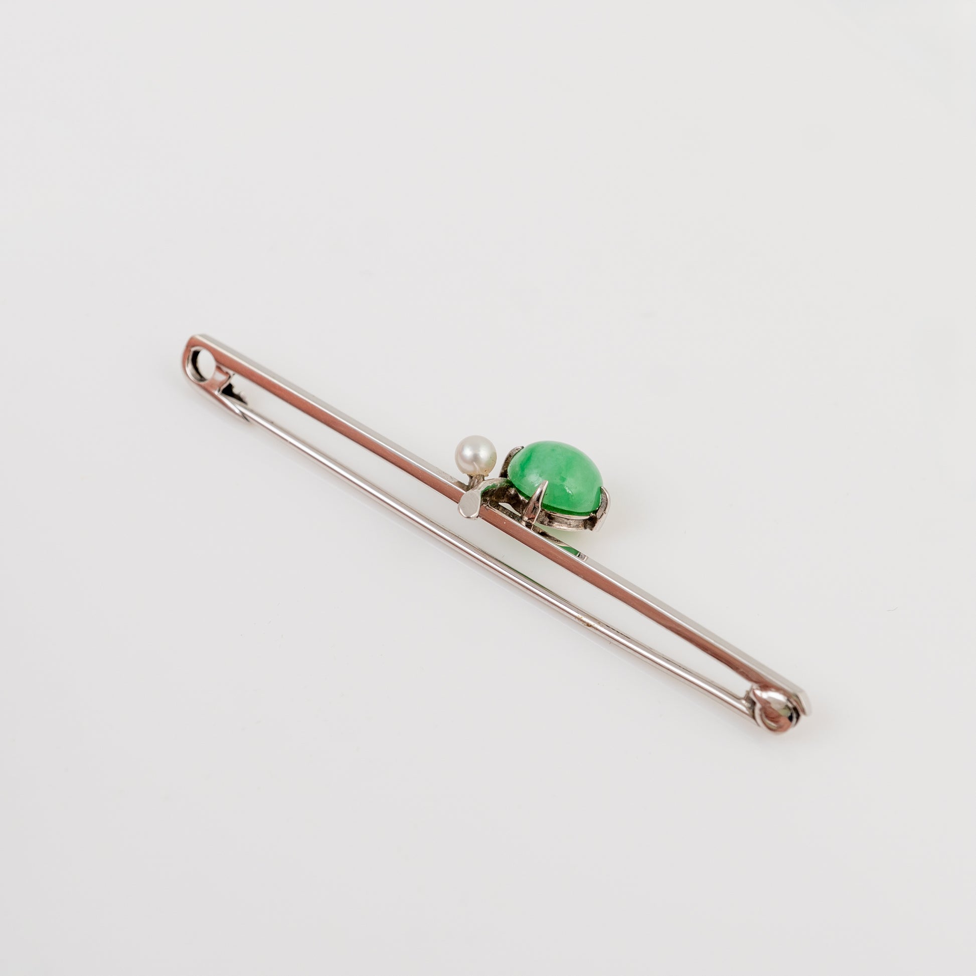 A silver-toned bar pin featuring a polished green oval hade cabochon and a small white pearl, displayed on a clean white background.