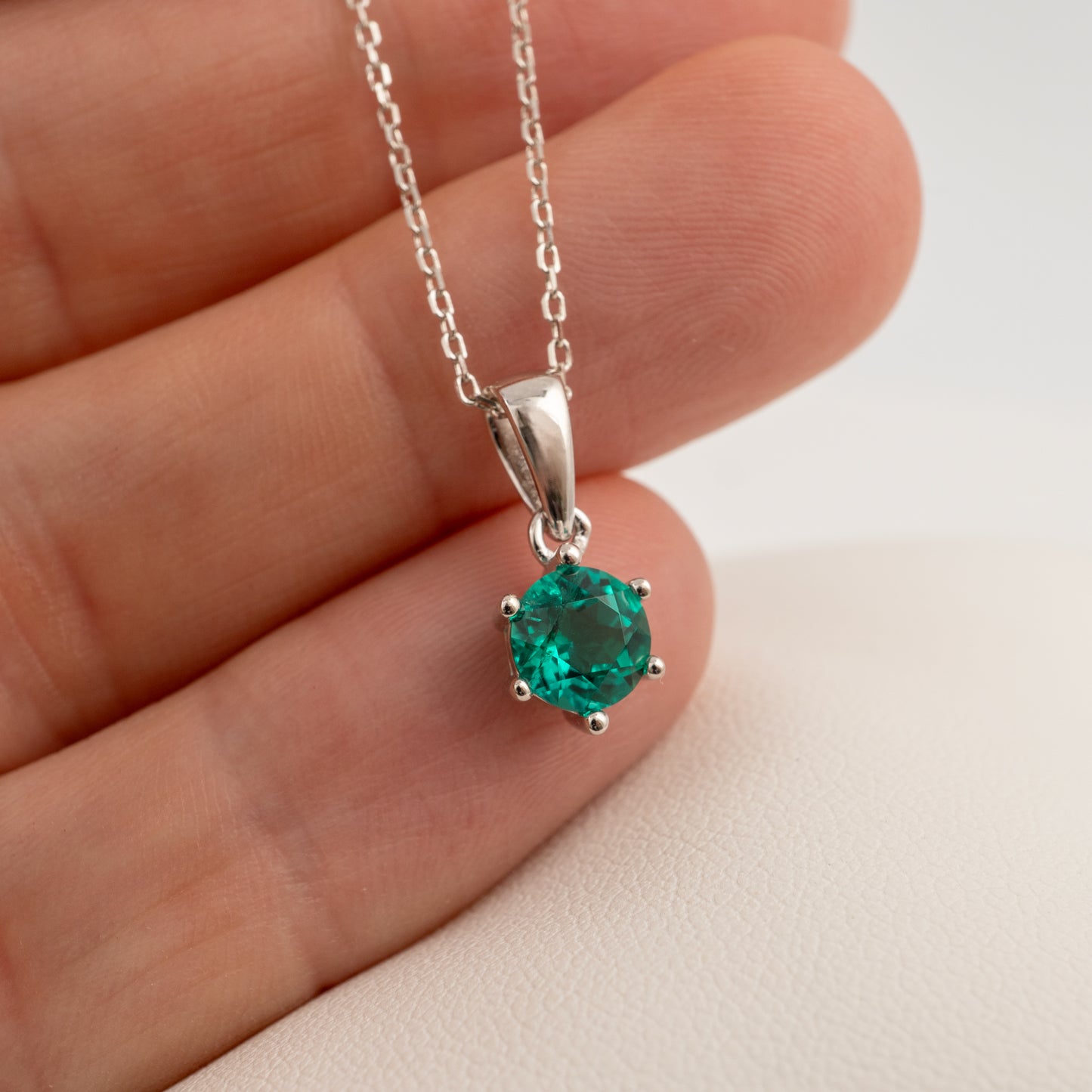 A sterling silver pendant necklace with a round-cut green gemstone, held in the palm of a hand against a light background.