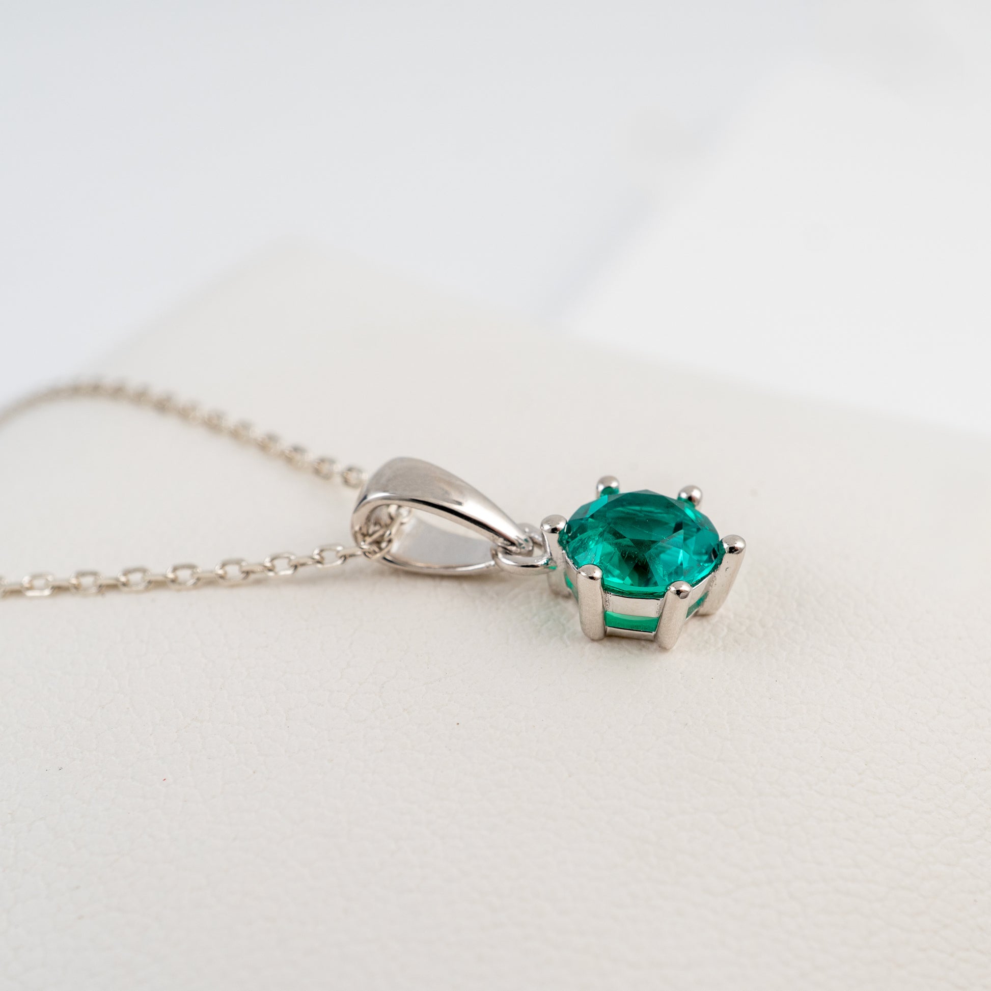 lab grown emerald necklace in a silver prong setting, resting on a textured white surface.